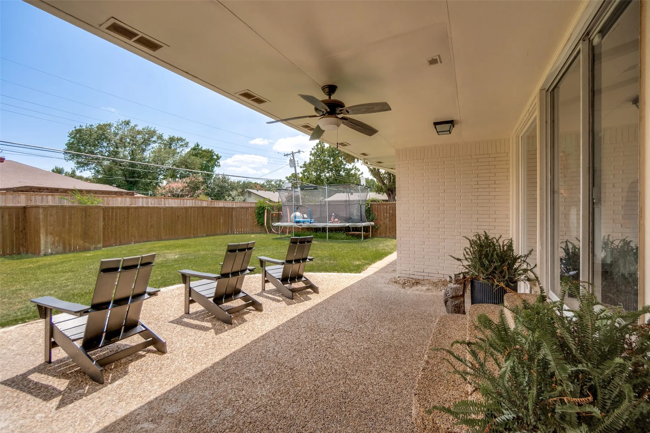 Covered patio with a ceiling fan, exposed aggregate concrete flooring, and a white brick exterior