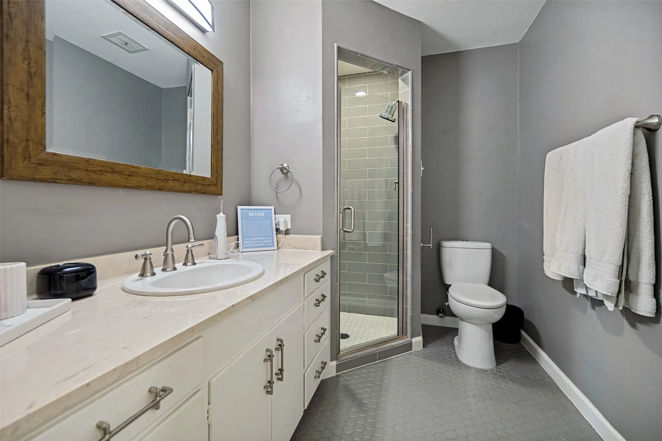 Bathroom featuring an extended vanity with an integrated sink, framed mirror, walk-in shower with subway tile surround, and hexagonal floor tiling