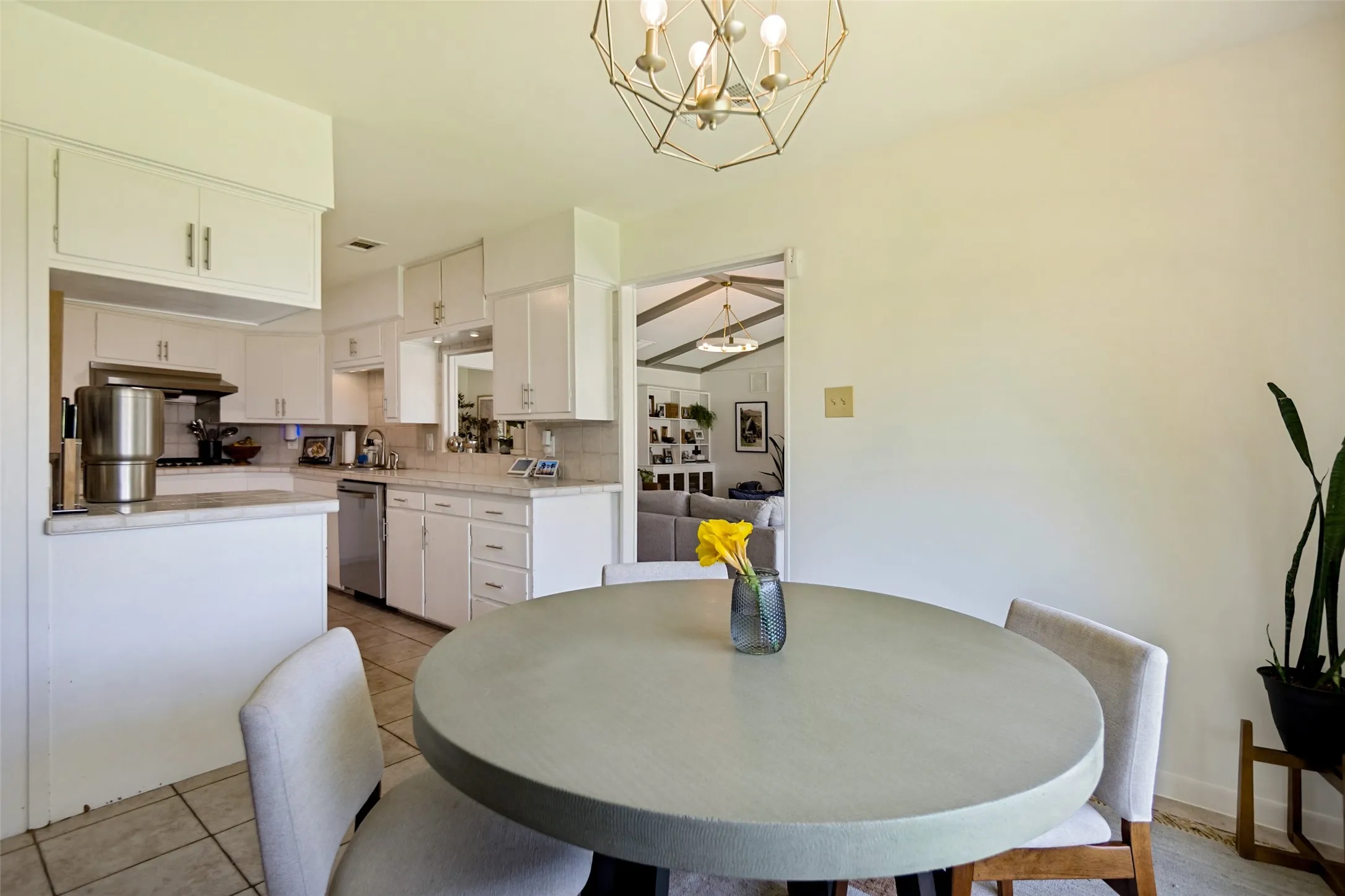 Contemporary geometric chandelier, white cabinetry with silver-tone hardware, light-toned countertops, stainless steel dishwasher, and tiled flooring