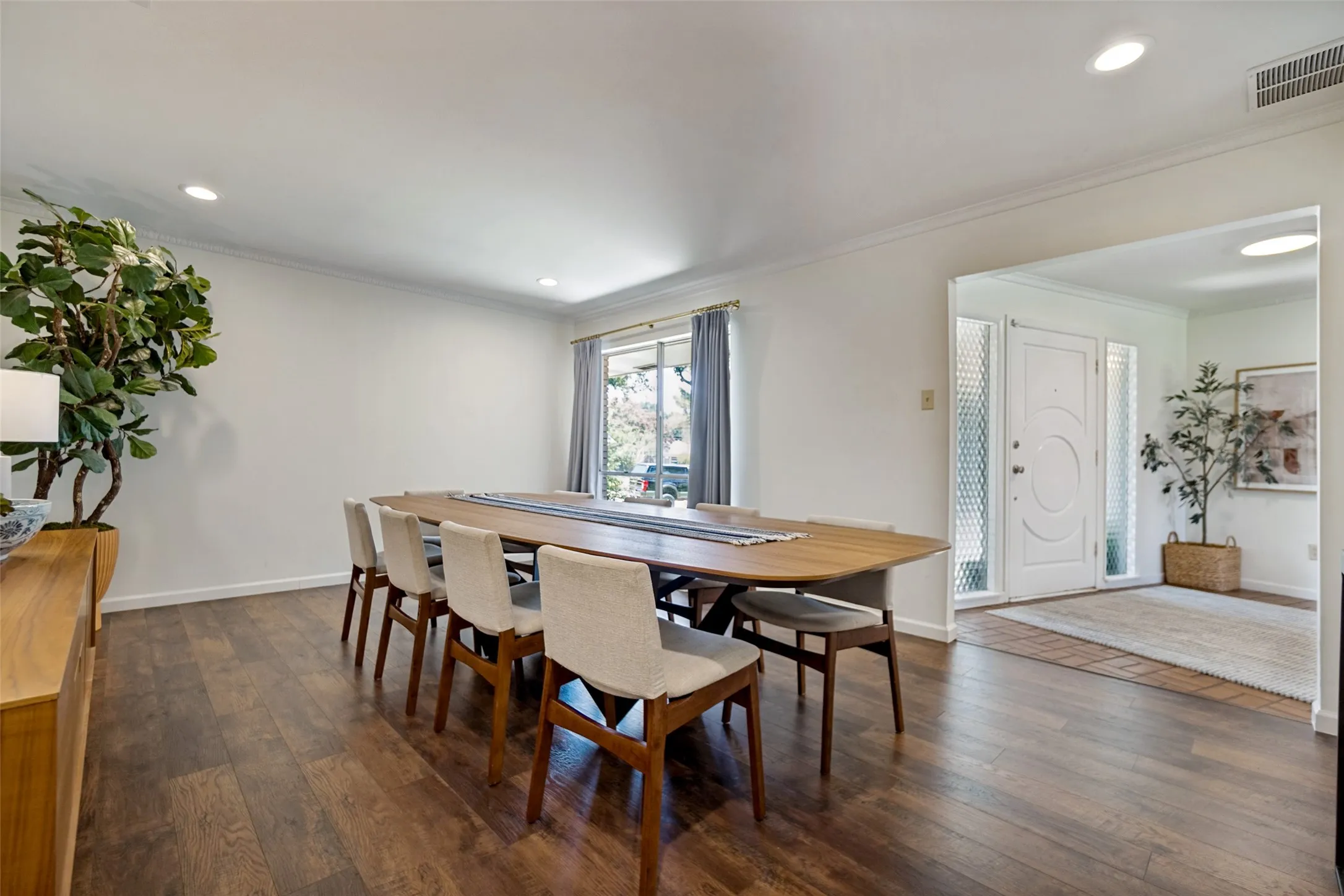 Hardwood-finish flooring throughout, recessed lighting, crown molding, and a bright white entry door with frosted glass sidelights