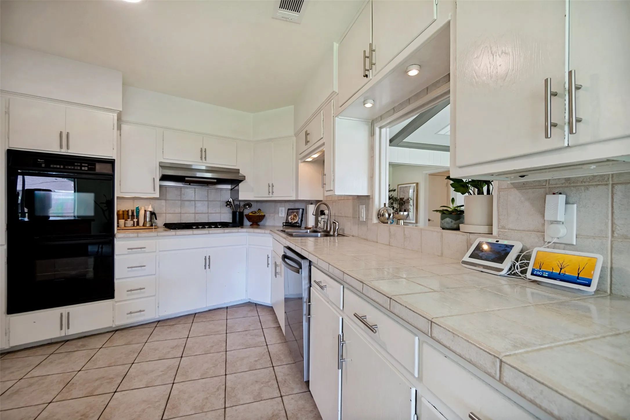 Kitchen featuring white cabinetry, tile countertops, integrated double oven, stainless steel dishwasher, and a tile backsplash
