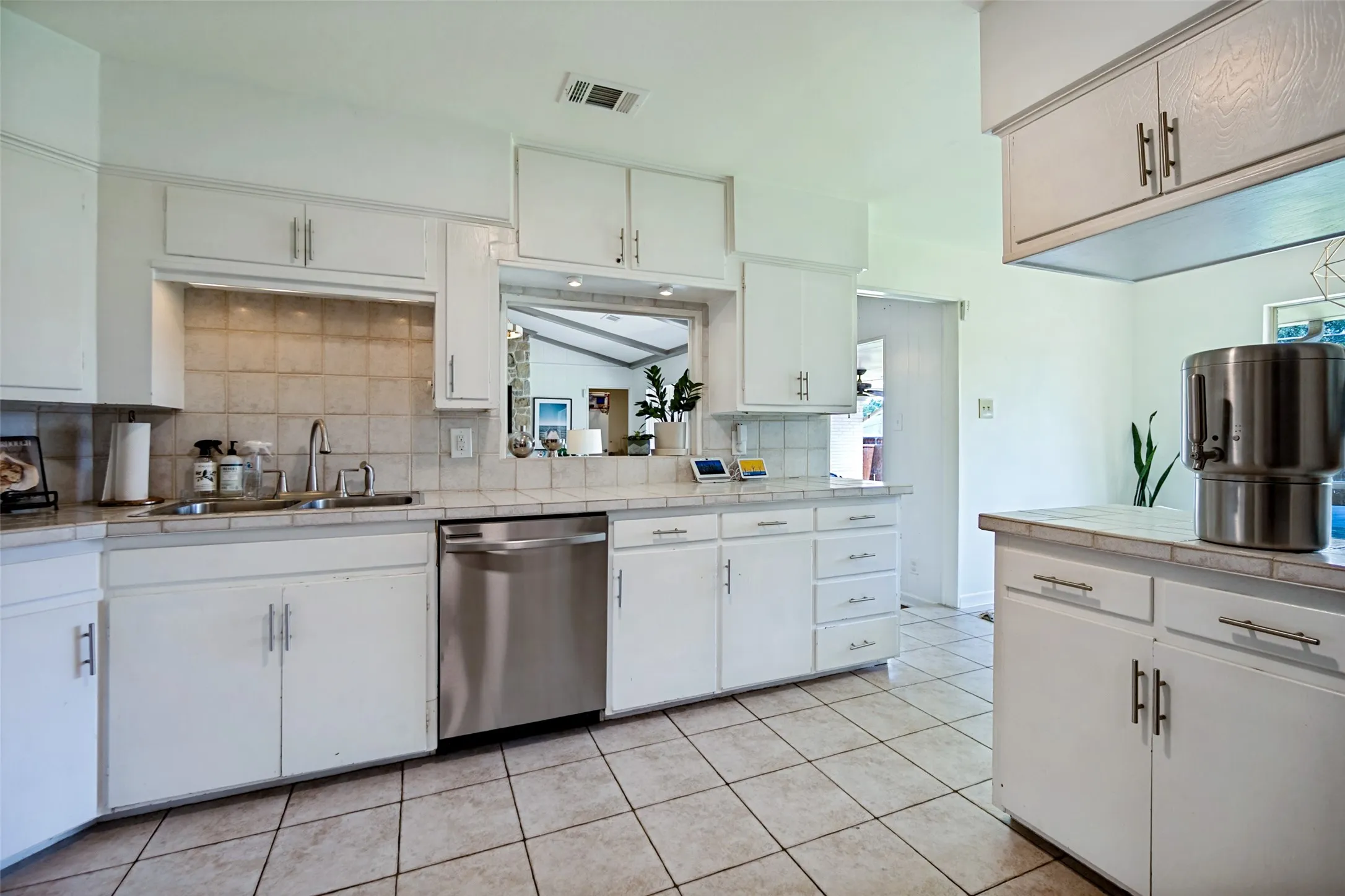 Kitchen featuring white cabinetry, tile countertops, tile flooring, and a stainless steel dishwasher