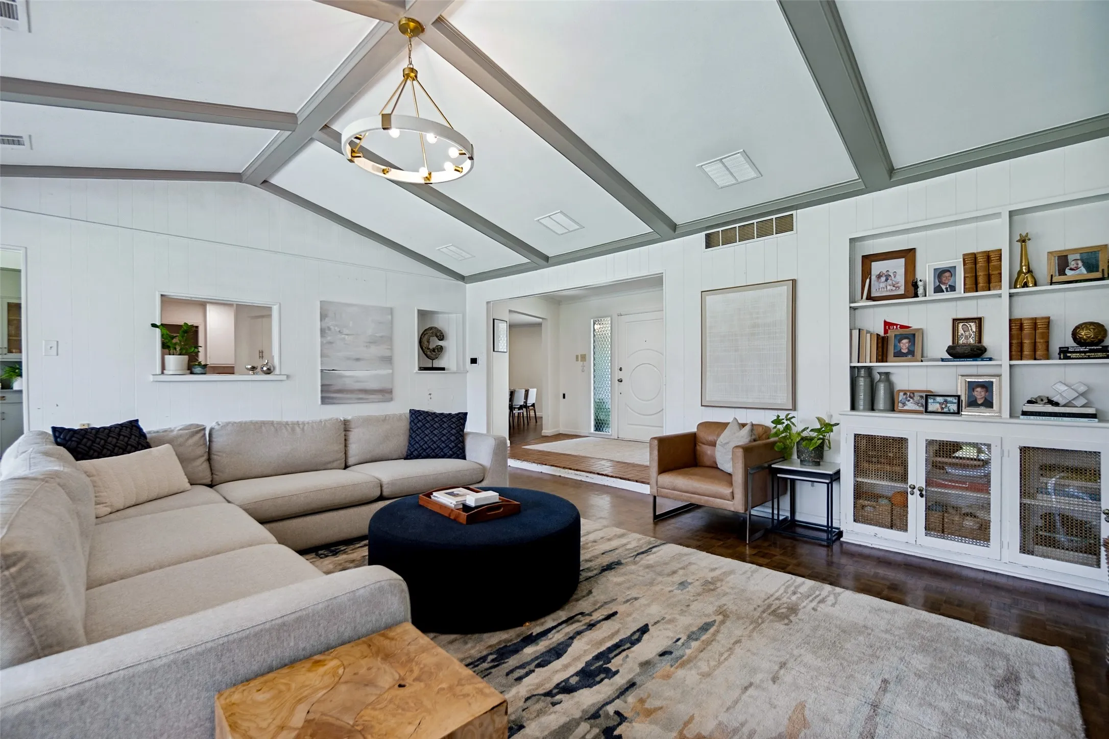 Vaulted ceiling with exposed beams, wood-finish flooring, built-in shelving, and a decorative chandelier