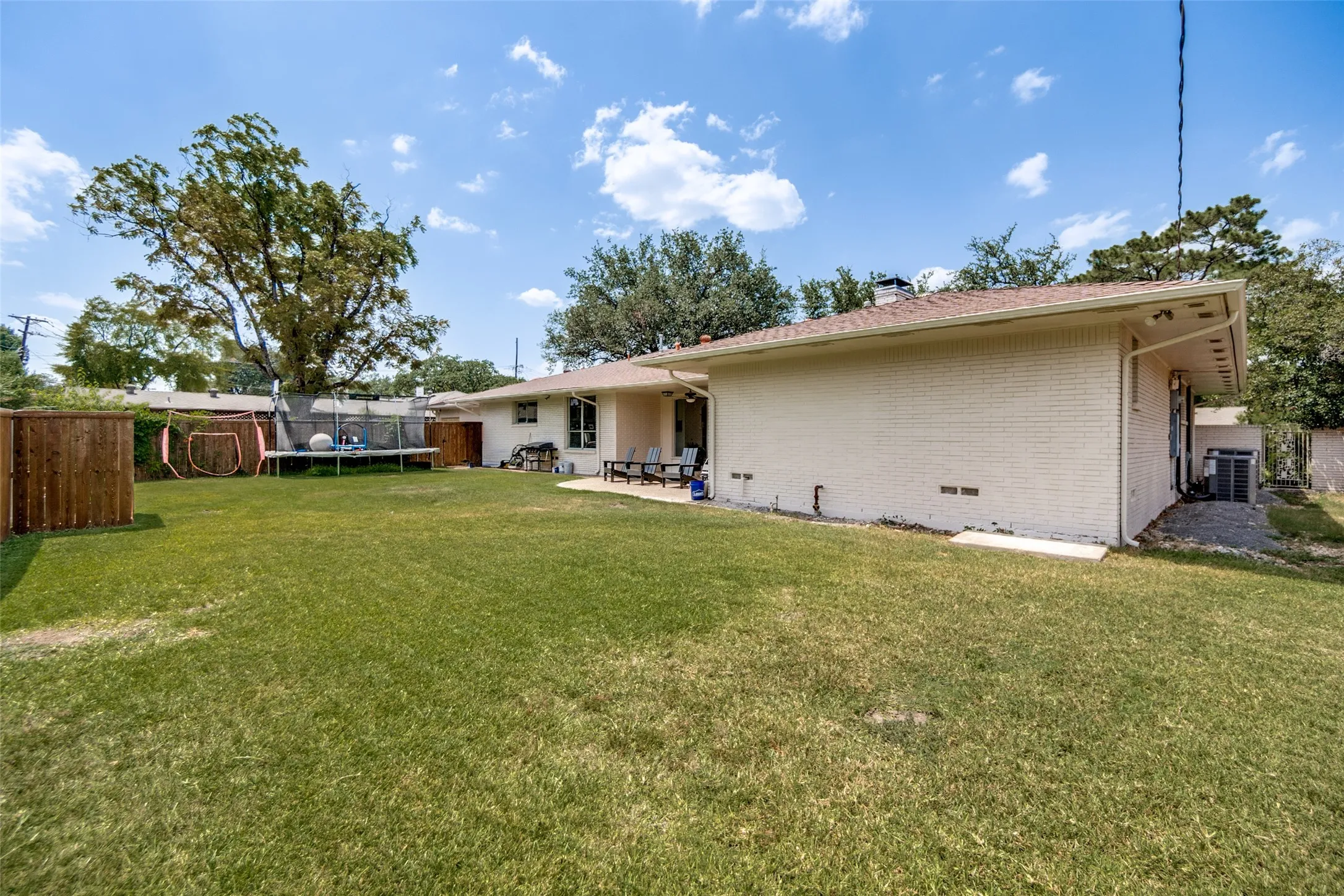 Expansive backyard with a manicured lawn, established trees, and a wooden privacy fence