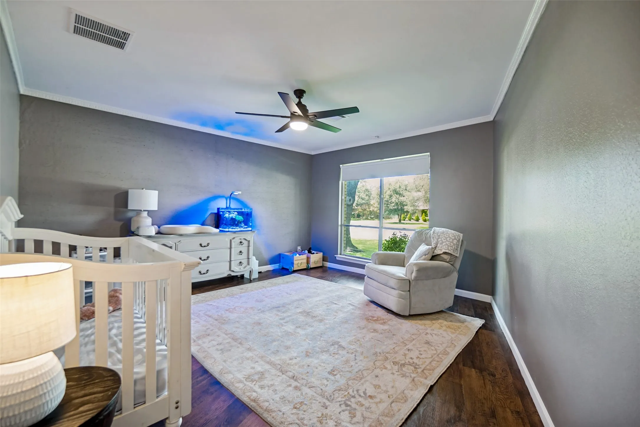 Warm wood-finish flooring, a large window, and crown molding enhance this room