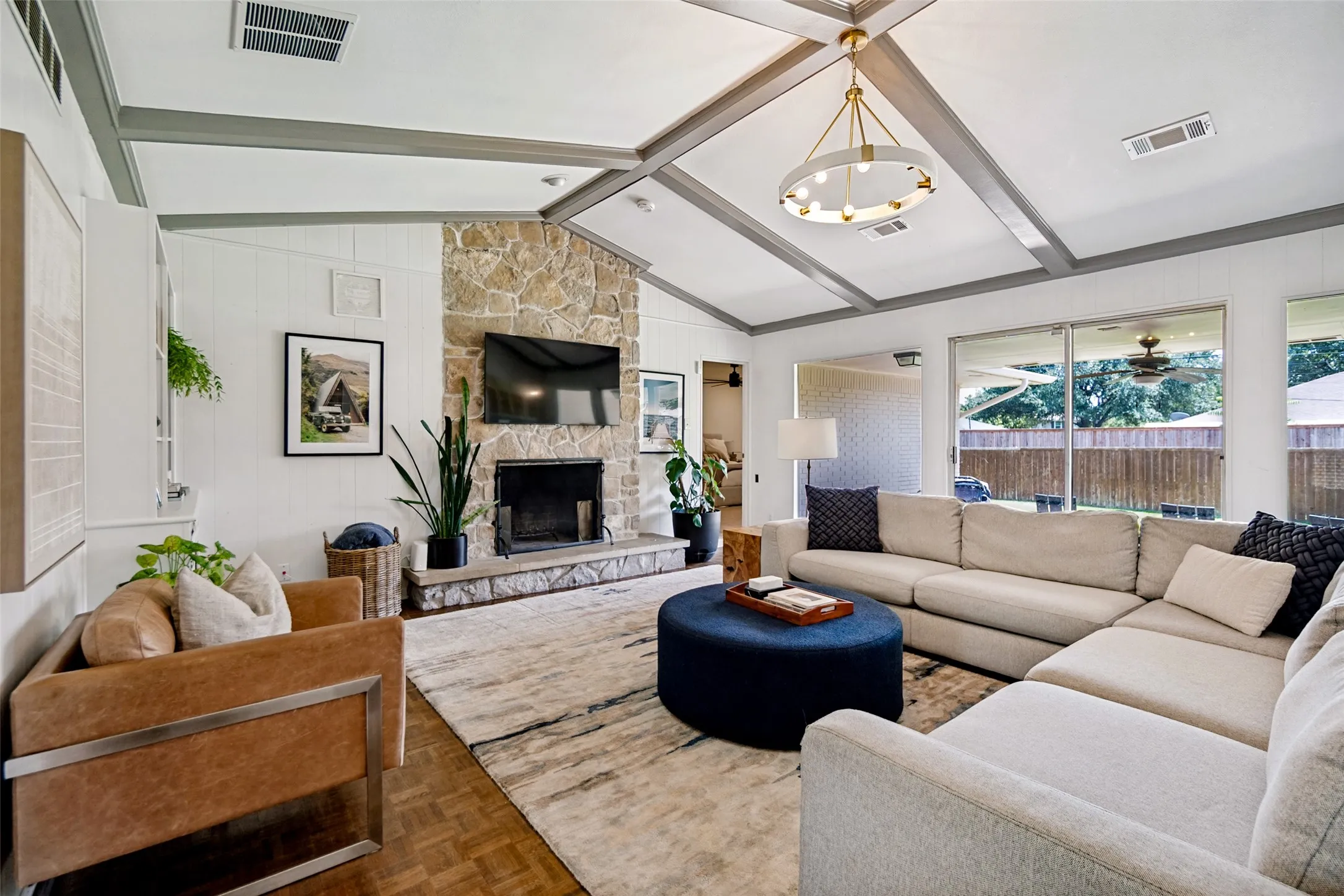 Vaulted ceiling with exposed beams, stone fireplace, wood-finish flooring, and expansive windows