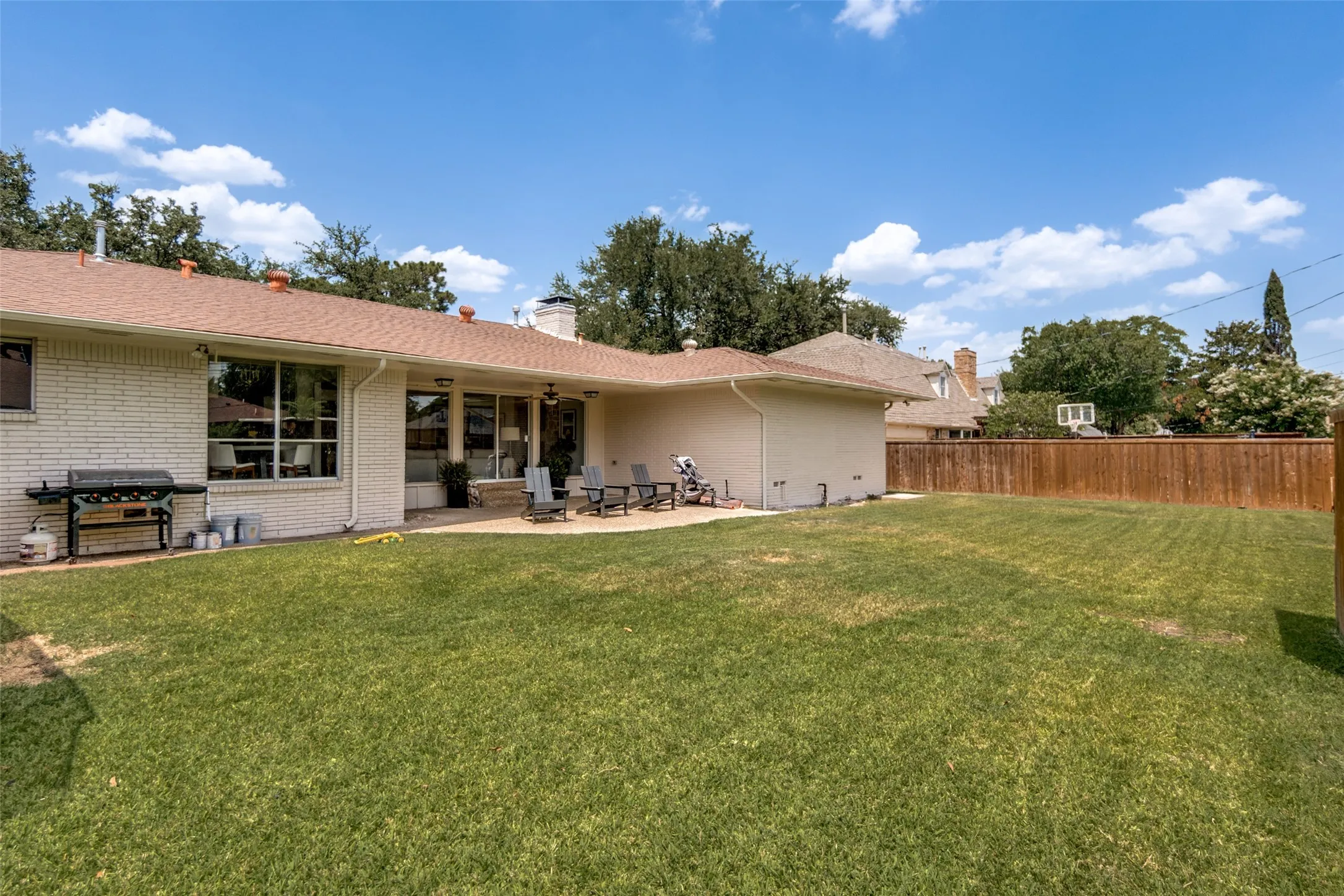 Expansive backyard featuring a large green lawn, concrete patio, and privacy fencing