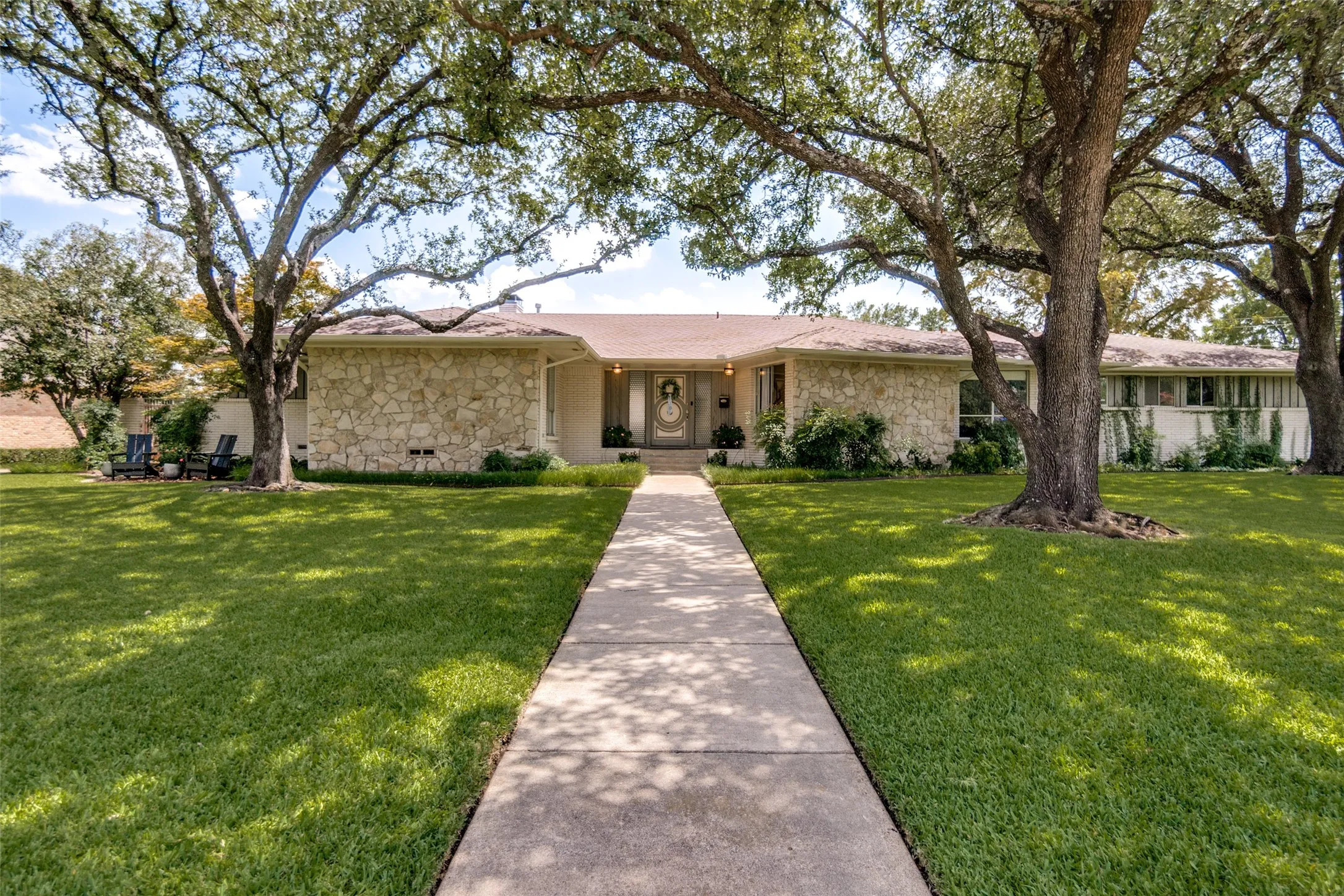 Stone facade exterior with a concrete walkway and mature trees
