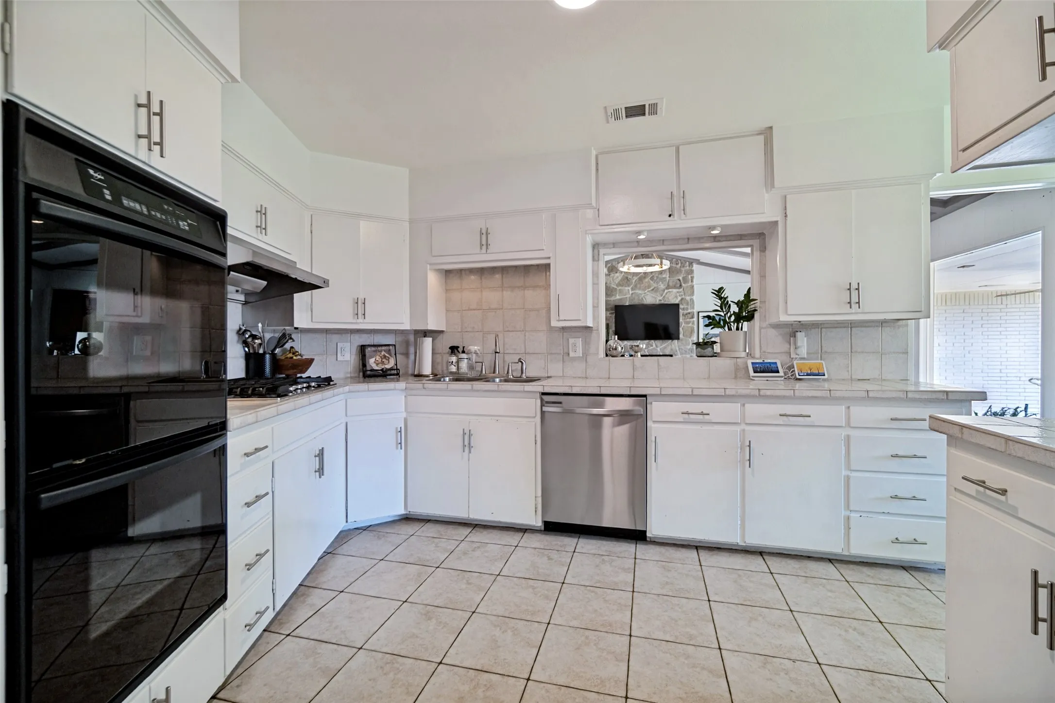 Kitchen featuring white cabinetry with brushed nickel hardware, stainless steel appliances, tile flooring, and a tile backsplash