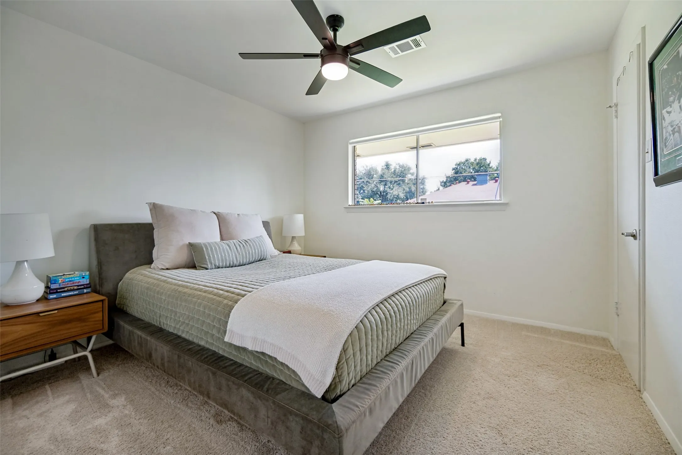Plush carpeted flooring, a ceiling fan with integrated lighting, and a window providing natural illumination