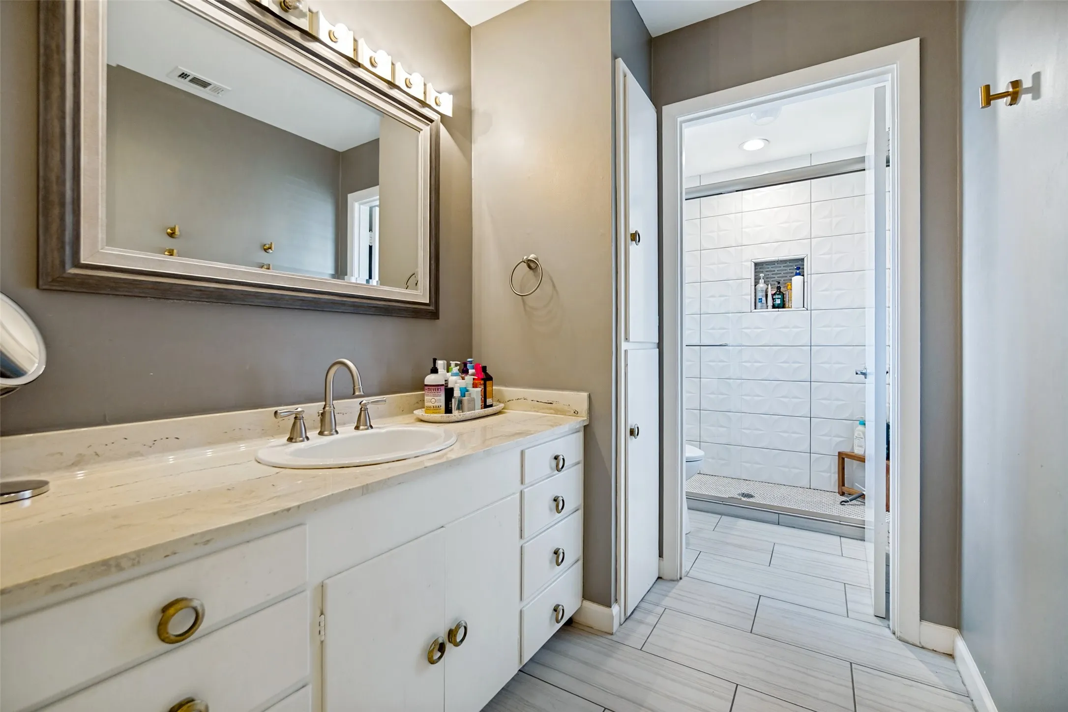 White vanity with brass-finish hardware, light-toned countertop, and undermount sink
