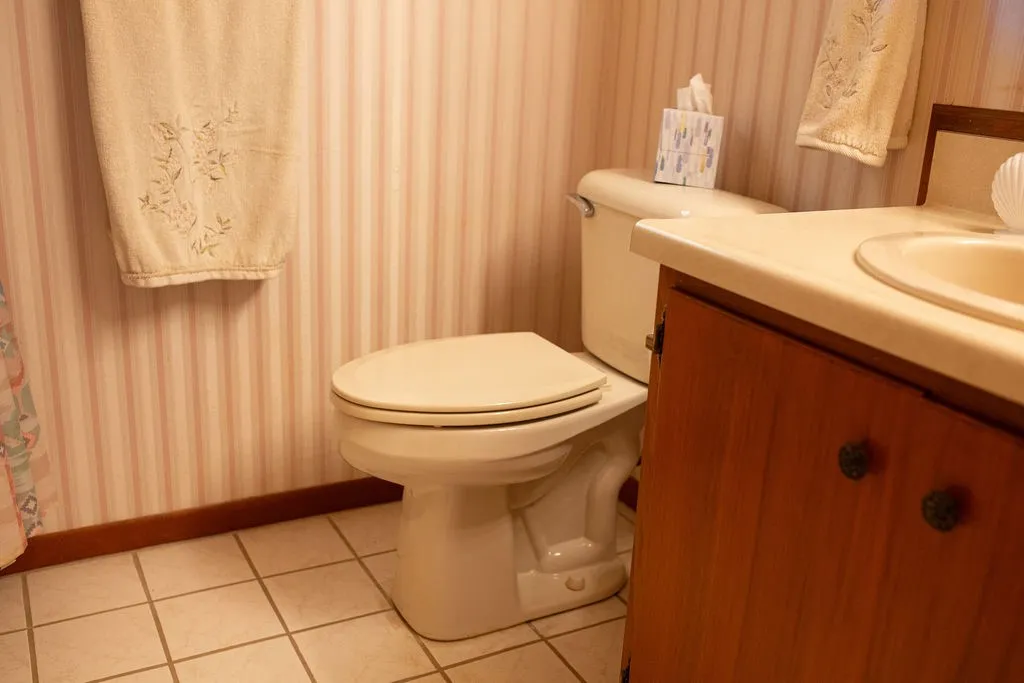White tile flooring, striped wallpaper, wood-finish vanity, and integrated sink