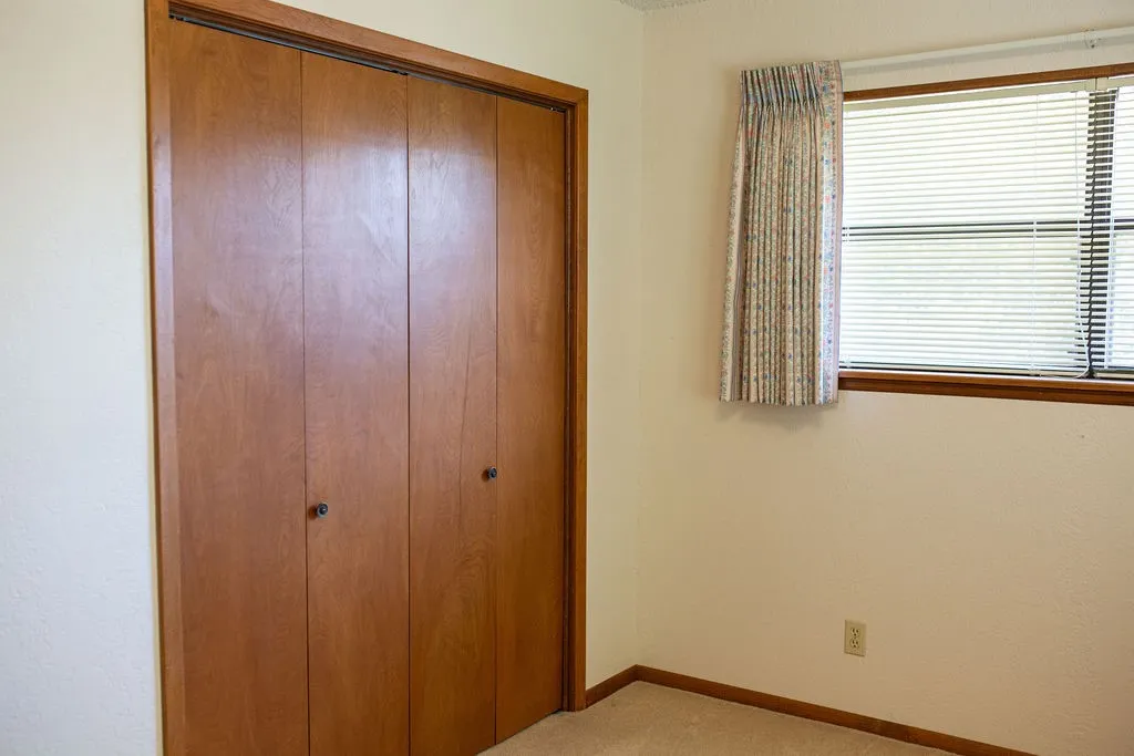 Wood-finish bi-fold doors, wood-frame window, and wall-to-wall carpeting