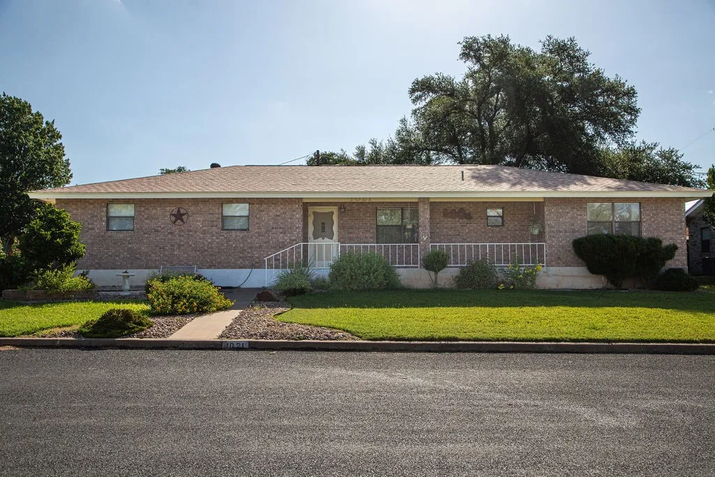 Brick exterior with a covered front porch featuring white railing, light brown shingles, and a paved walkway