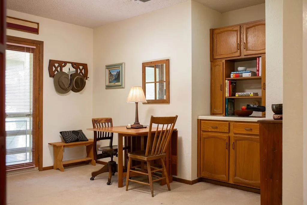 Warm wood-finish dining table with matching chairs, anchored by a table lamp with cream shade