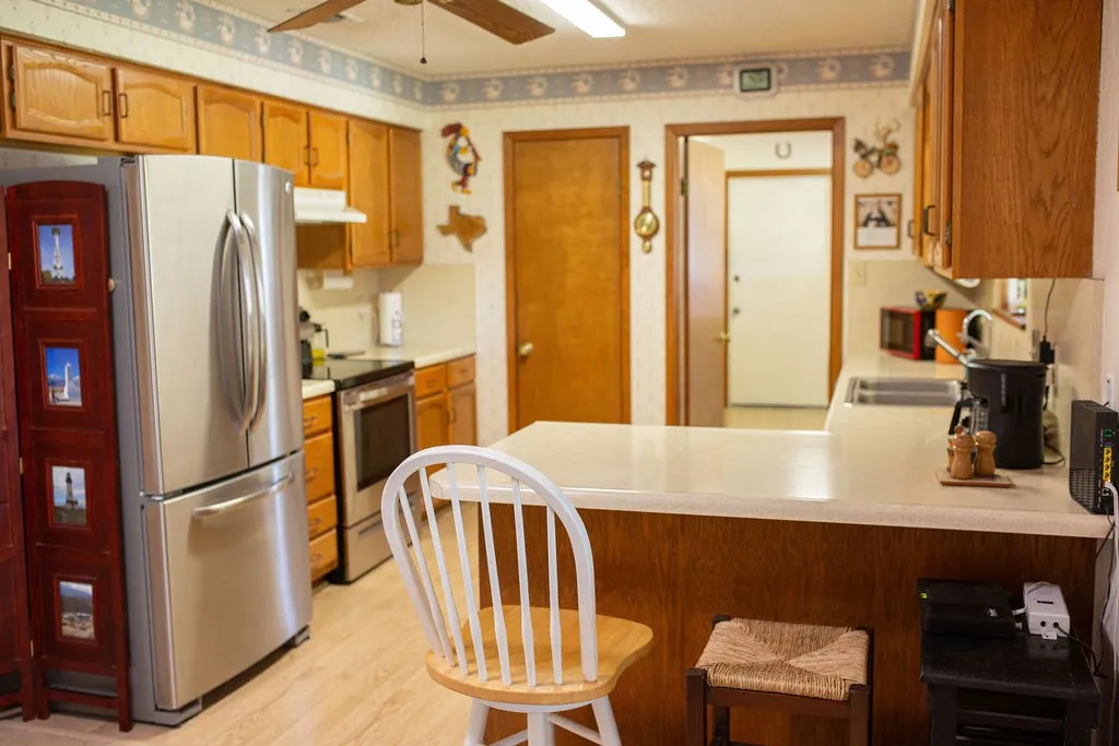 Light wood-finish cabinetry, stainless steel refrigerator, built-in range, wood-finish flooring, and a ceiling fan with light fixture