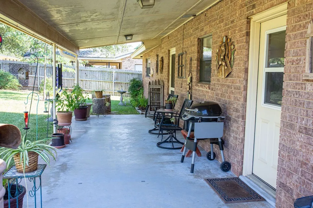 Covered concrete patio with a brick exterior, white framed door, and multiple windows
