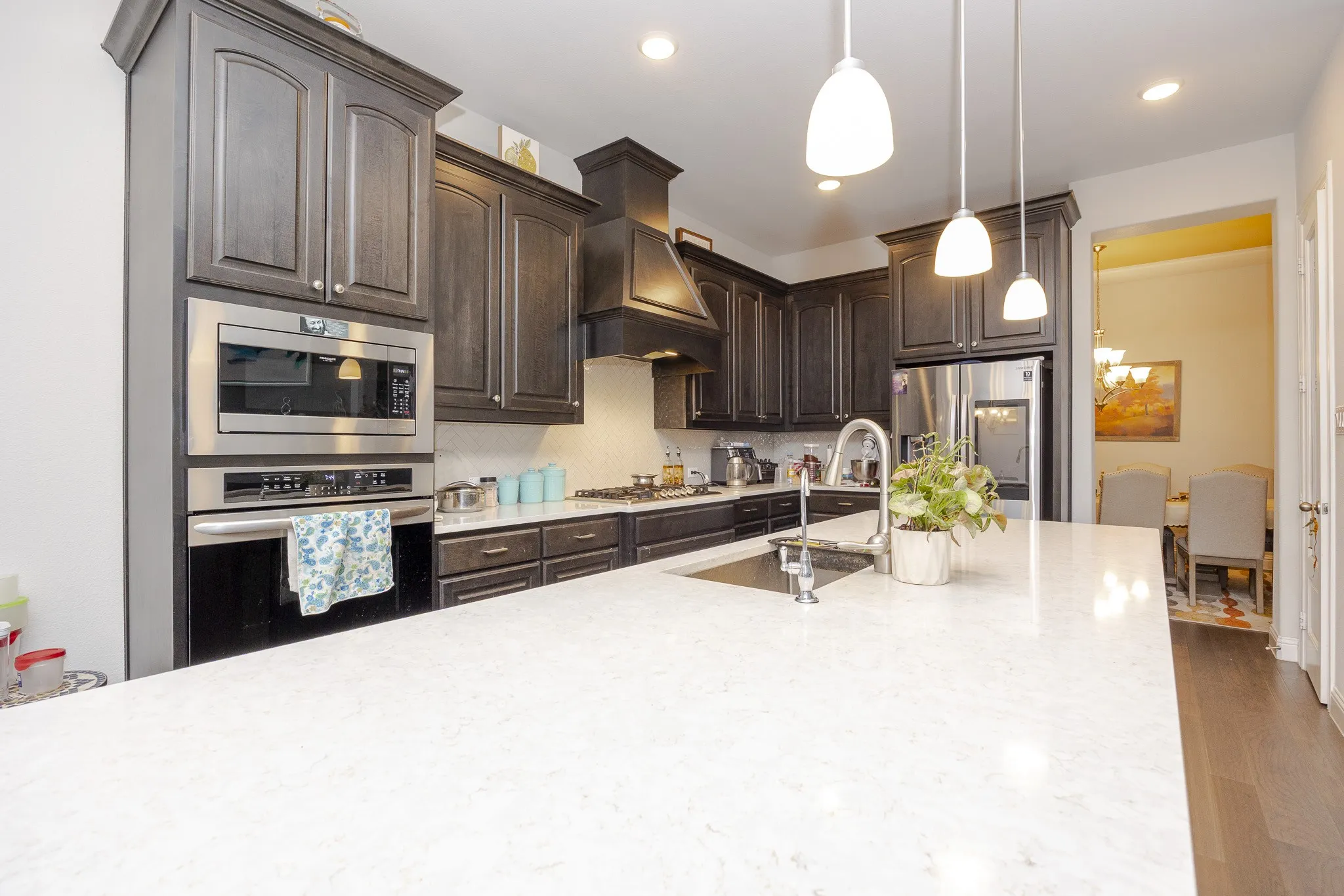 Spacious kitchen featuring an expansive island with an undermount sink, dark wood cabinetry with crown molding, stainless steel appliances, and pendant lighting