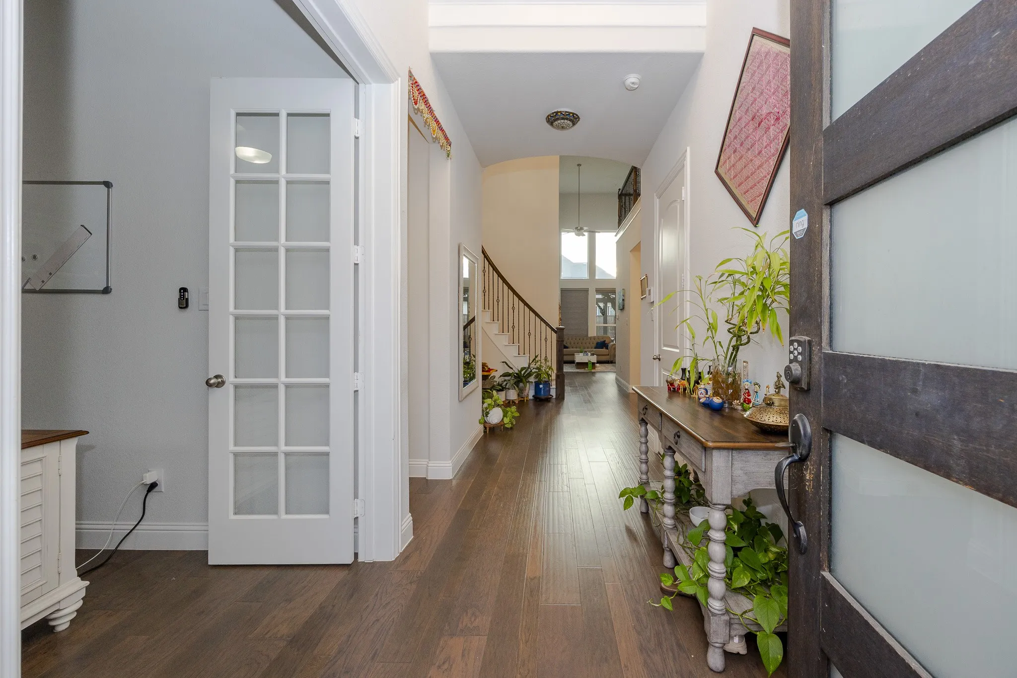 Wood-finish flooring throughout, with a white French door, a wooden staircase with white balusters, and a dark wood entry door with frosted glass panels