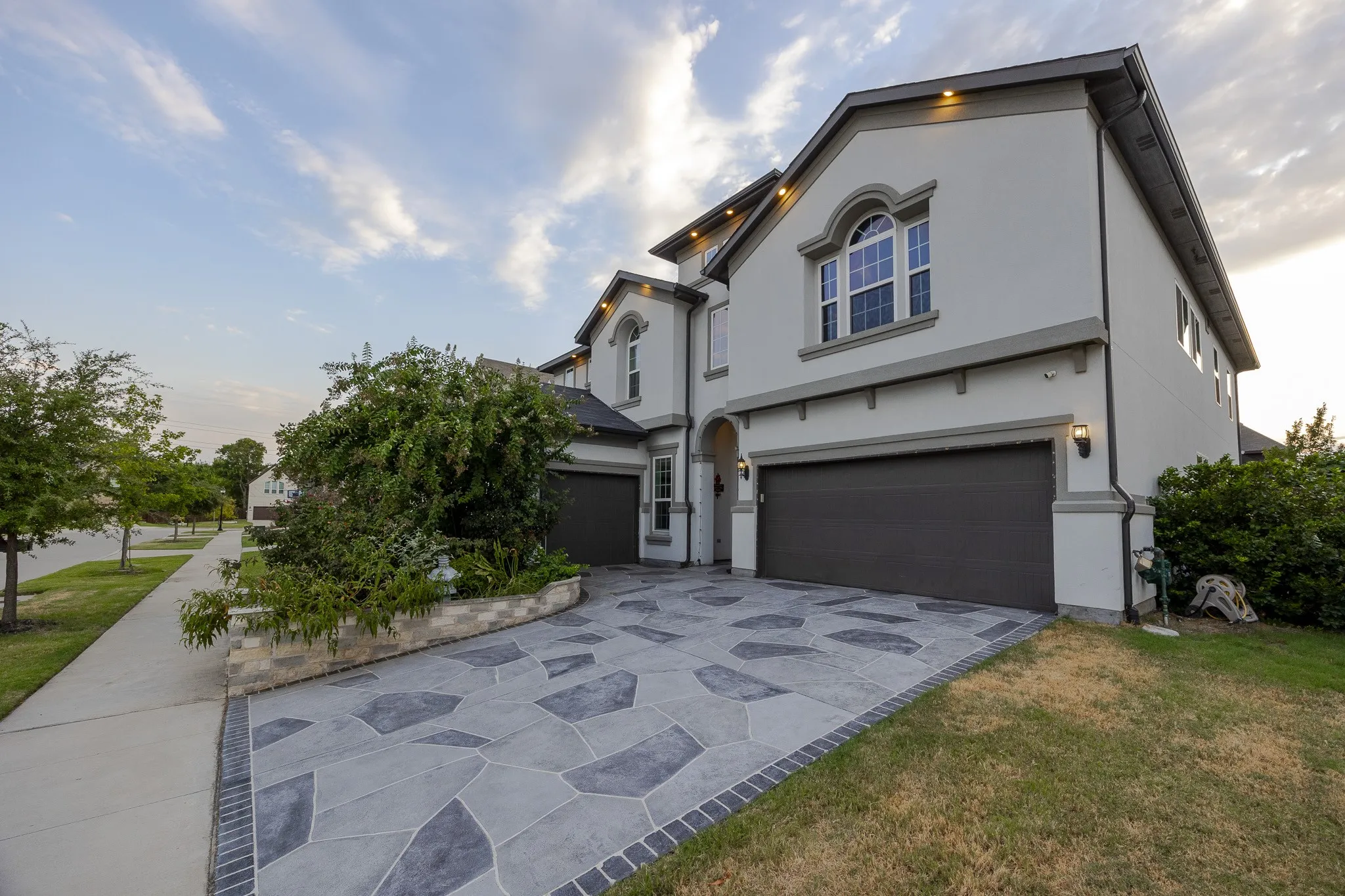 Stucco exterior with arched window casings, two-car garage, and an intricate stone-patterned driveway