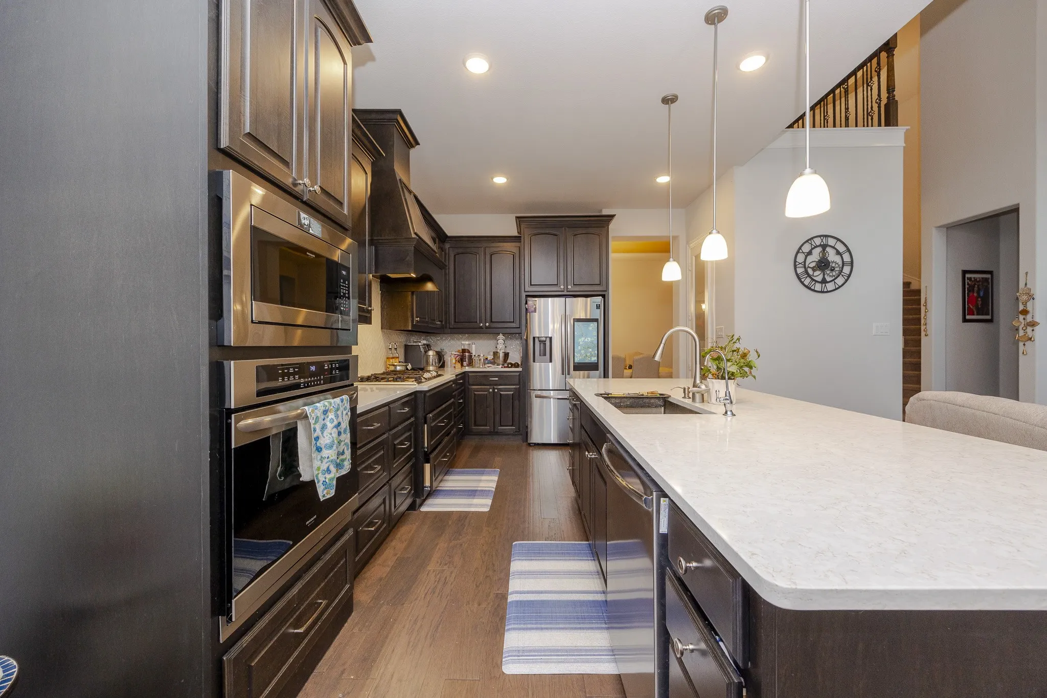 Gourmet kitchen featuring stainless steel appliances, dark wood-finish cabinetry, a large center island with a sink, and pendant lighting