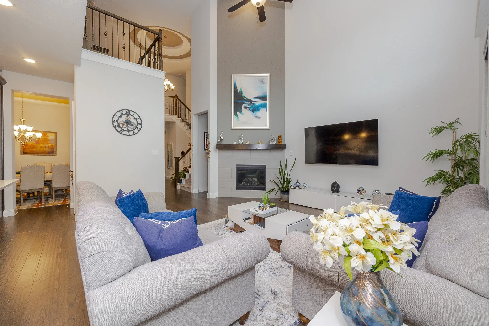 Two-story living area with high ceilings, fireplace with wood mantel, wood-finish flooring, and a wrought iron balcony