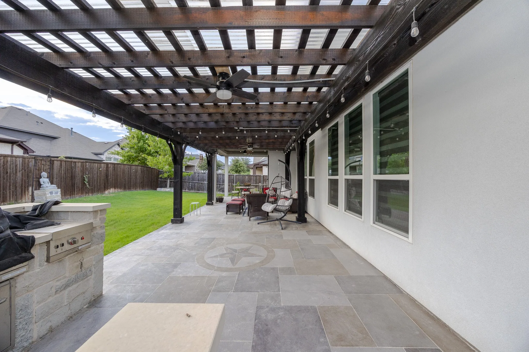 Expansive outdoor patio with a wood pergola, built-in outdoor kitchen, ceiling fans, and large-format tile flooring