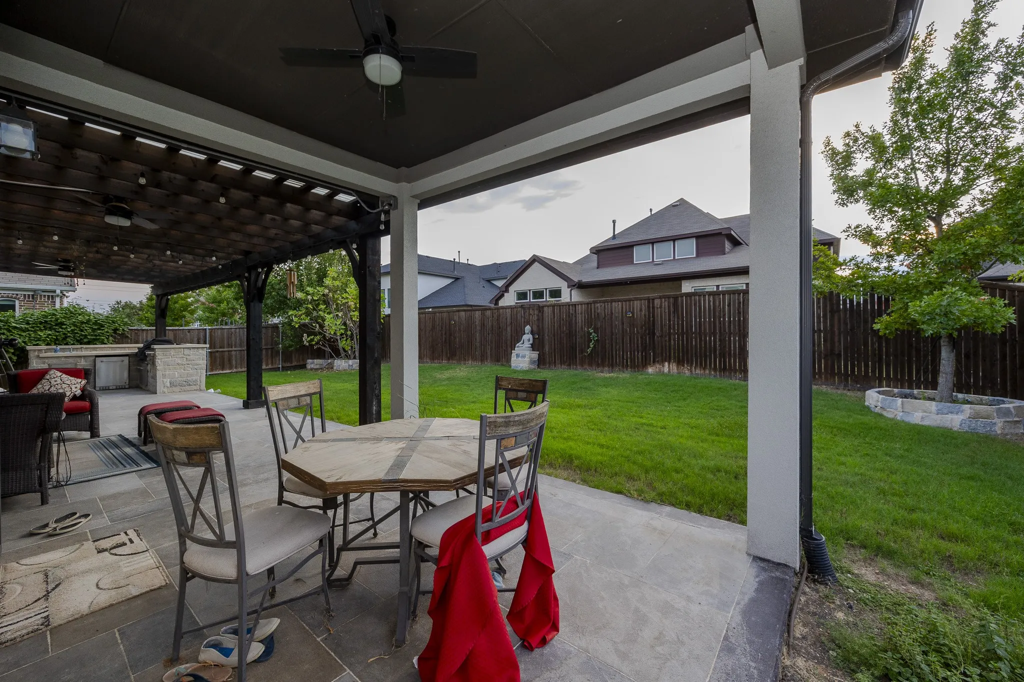 Expansive backyard featuring a covered patio with a ceiling fan, a pergola structure, a built-in outdoor kitchen, and a manicured lawn