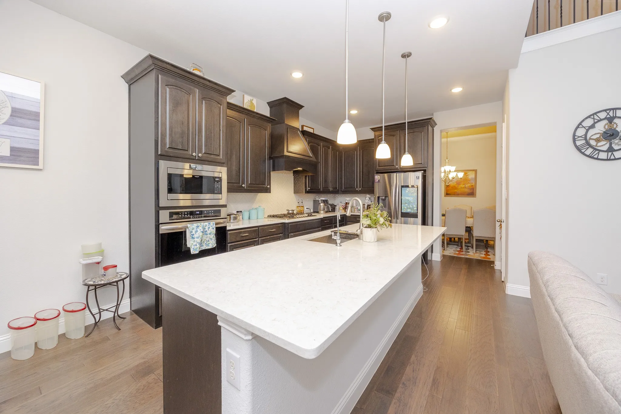 Spacious kitchen featuring an extended island with a white countertop, dark wood-finish cabinetry, stainless steel appliances, and pendant lighting