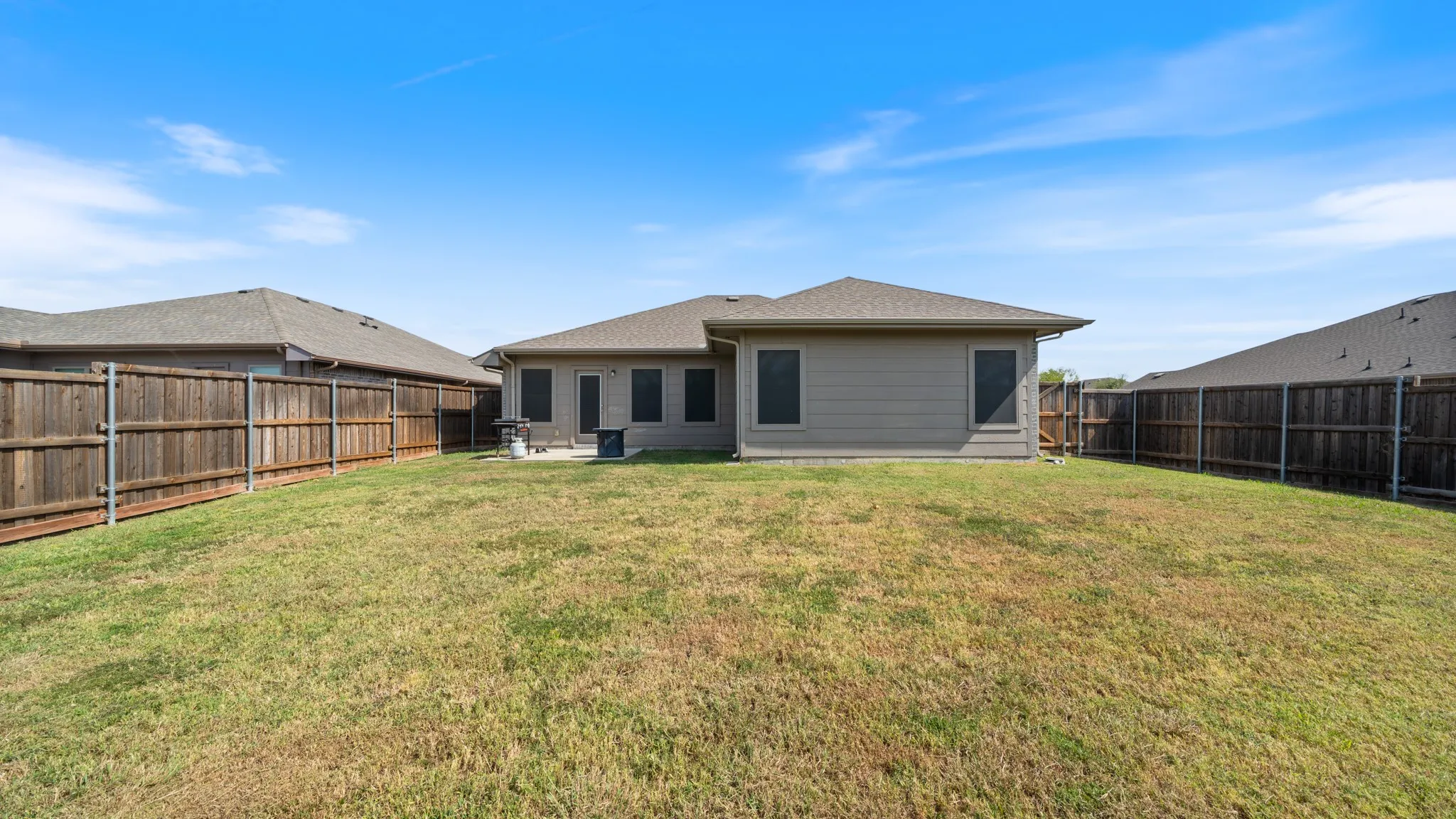 Expansive backyard featuring a manicured lawn, wood fencing, and a concrete patio