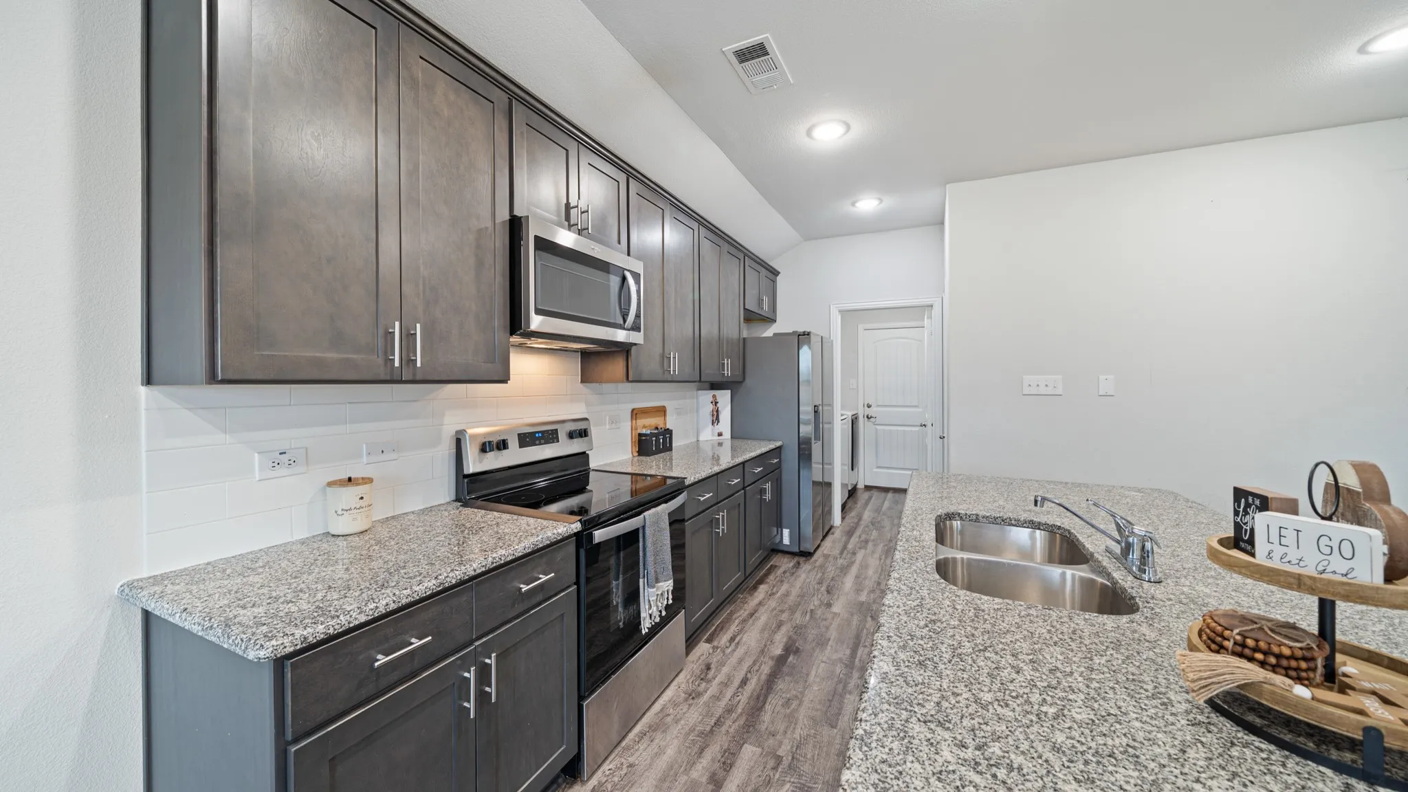 Kitchen featuring dark wood-finish cabinetry, light speckled countertops, a stainless steel double basin sink, a stainless steel microwave, and wood-finish flooring