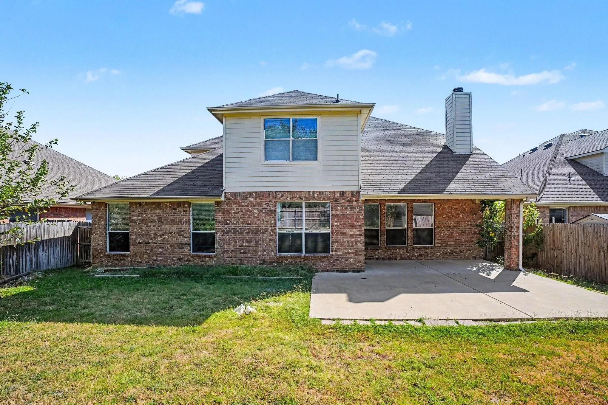 Expansive rear elevation featuring brick and siding, a covered patio, and a shingled roof