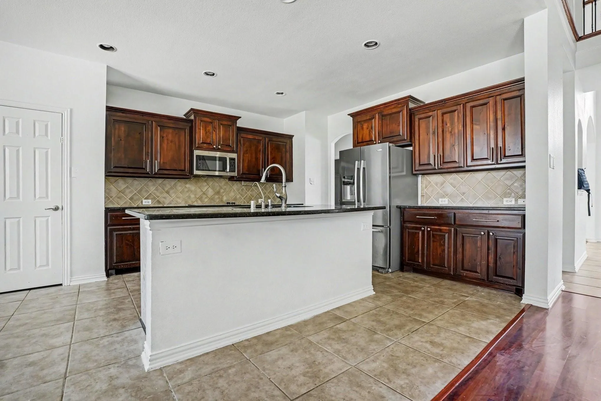 Kitchen featuring wood-finish cabinetry, stainless steel appliances, a center island with a sink, tile flooring, and recessed lighting