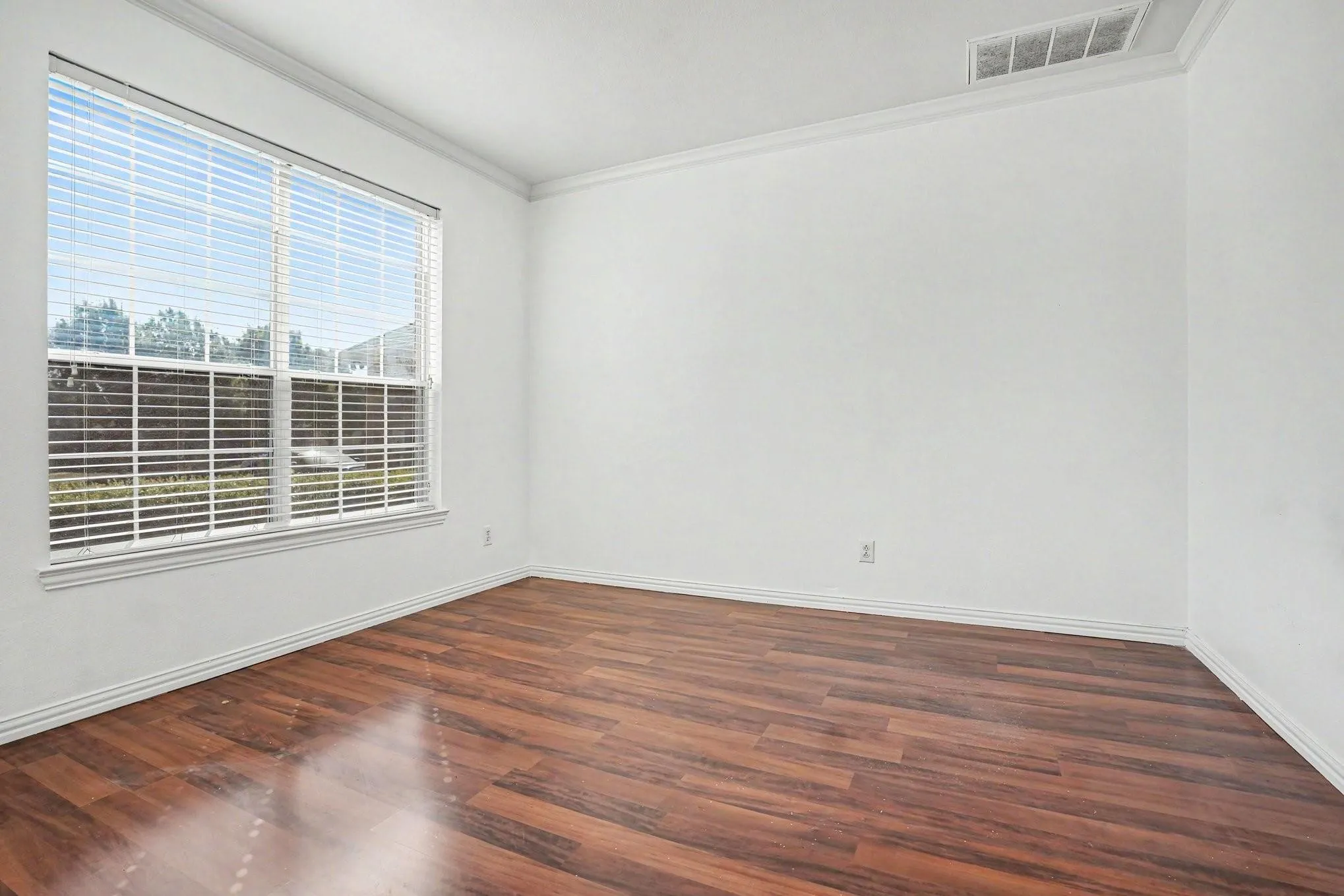 Wood-finish flooring, crown molding, a large window, and crisp white walls define this bright interior space