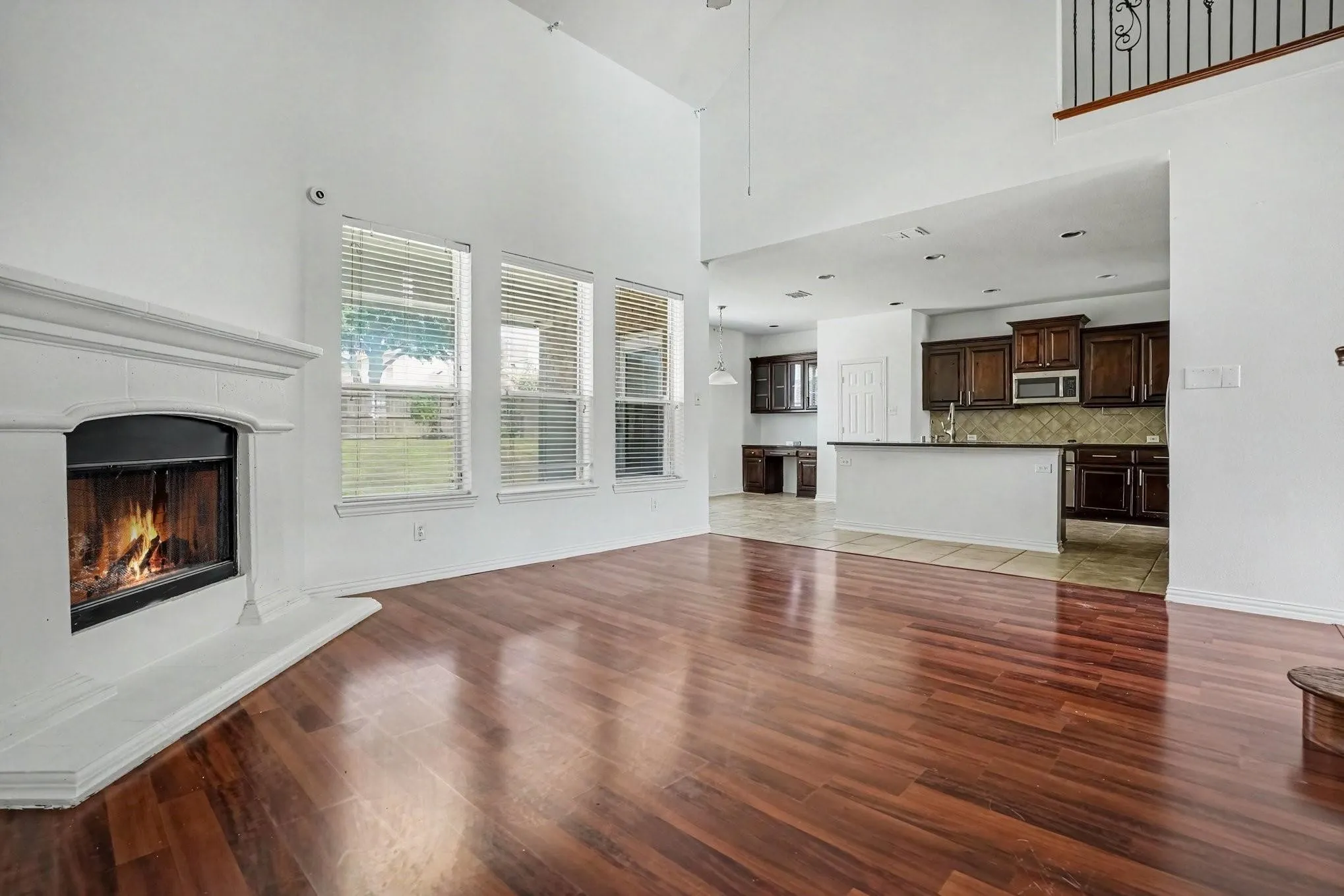 Two-story living area with high ceilings, wood-finish flooring, a white mantel fireplace, and multiple windows