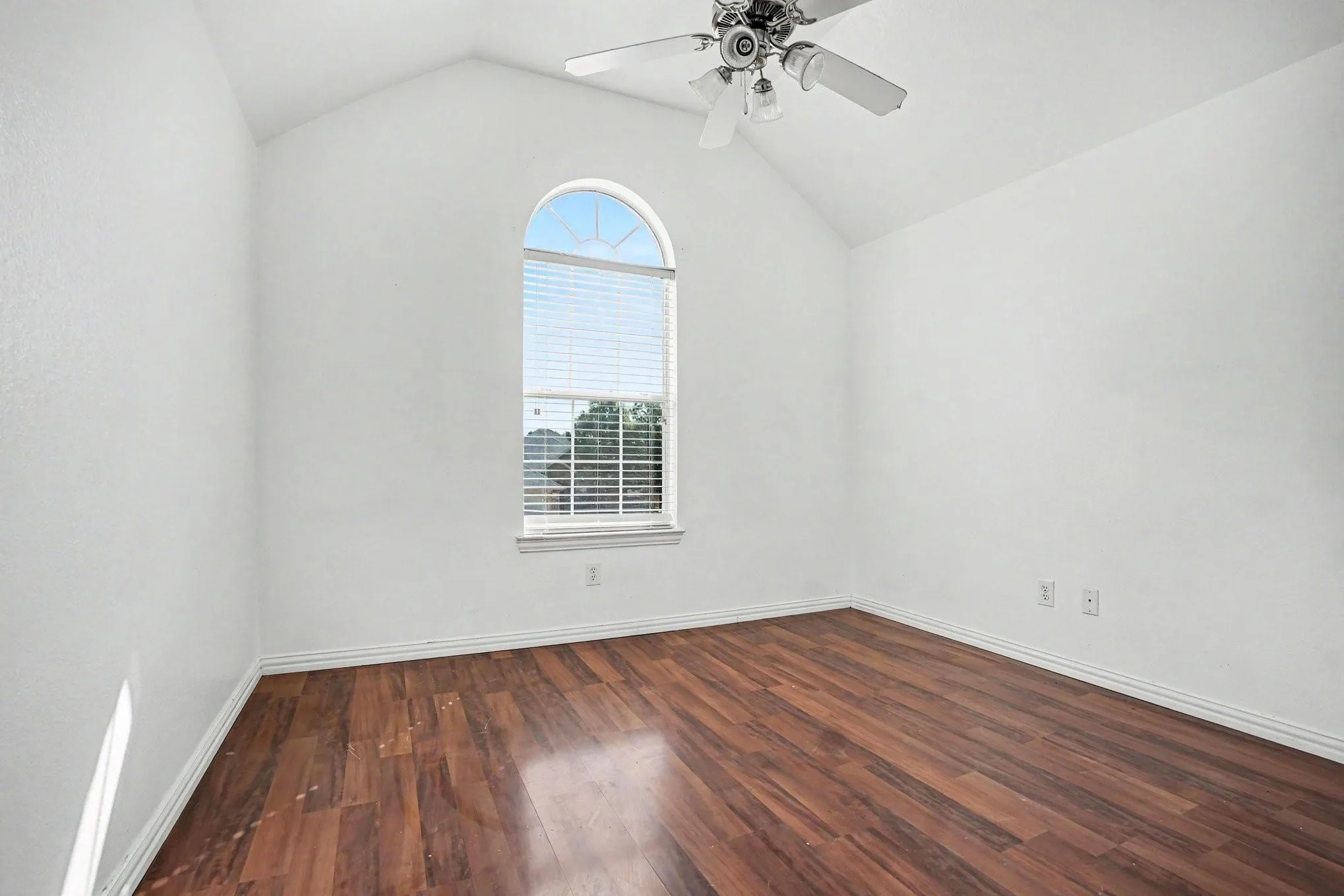 Arched window with blinds, wood-finish flooring, vaulted ceiling, and ceiling fan