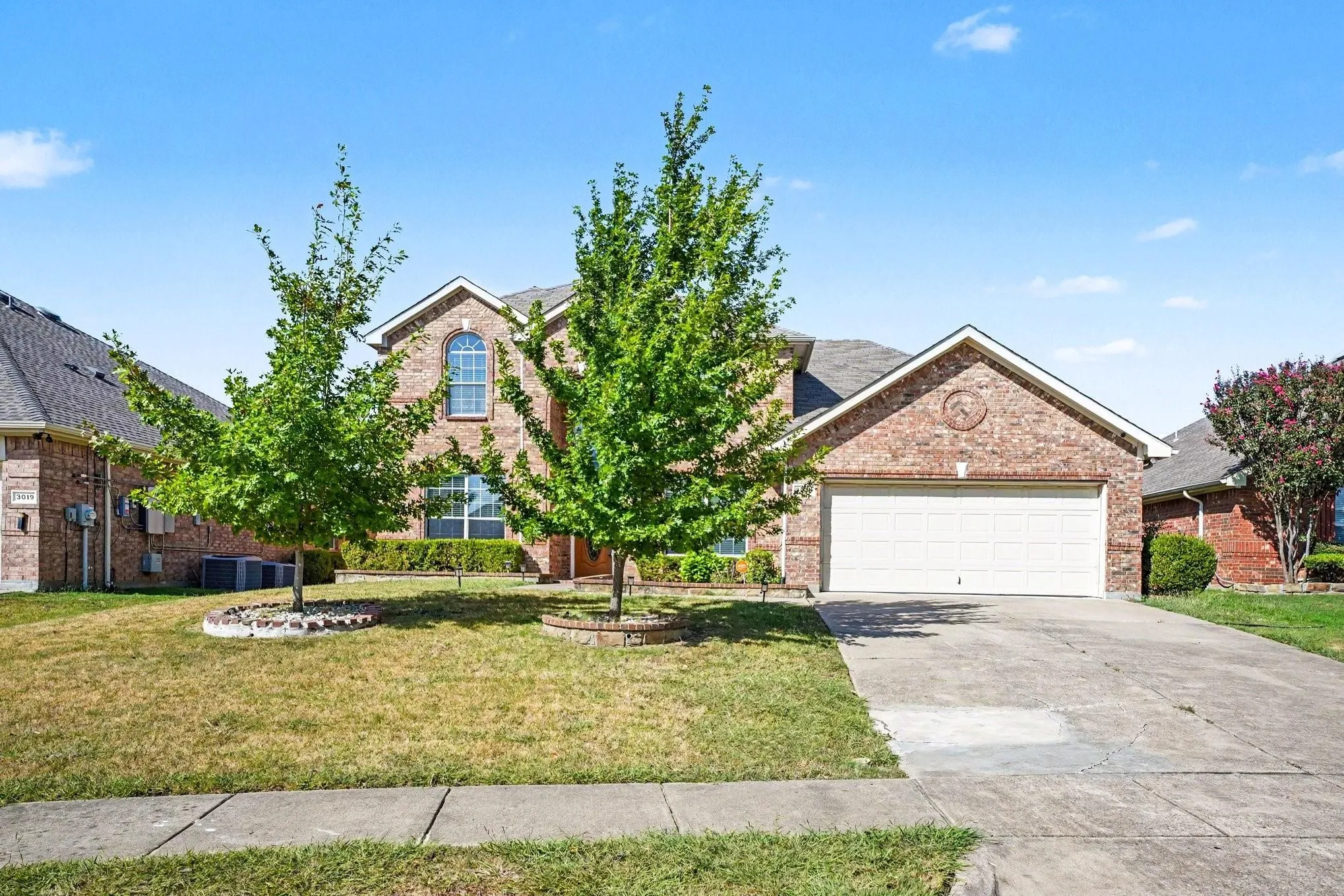 Brick exterior with an arched window, attached garage, and a concrete driveway