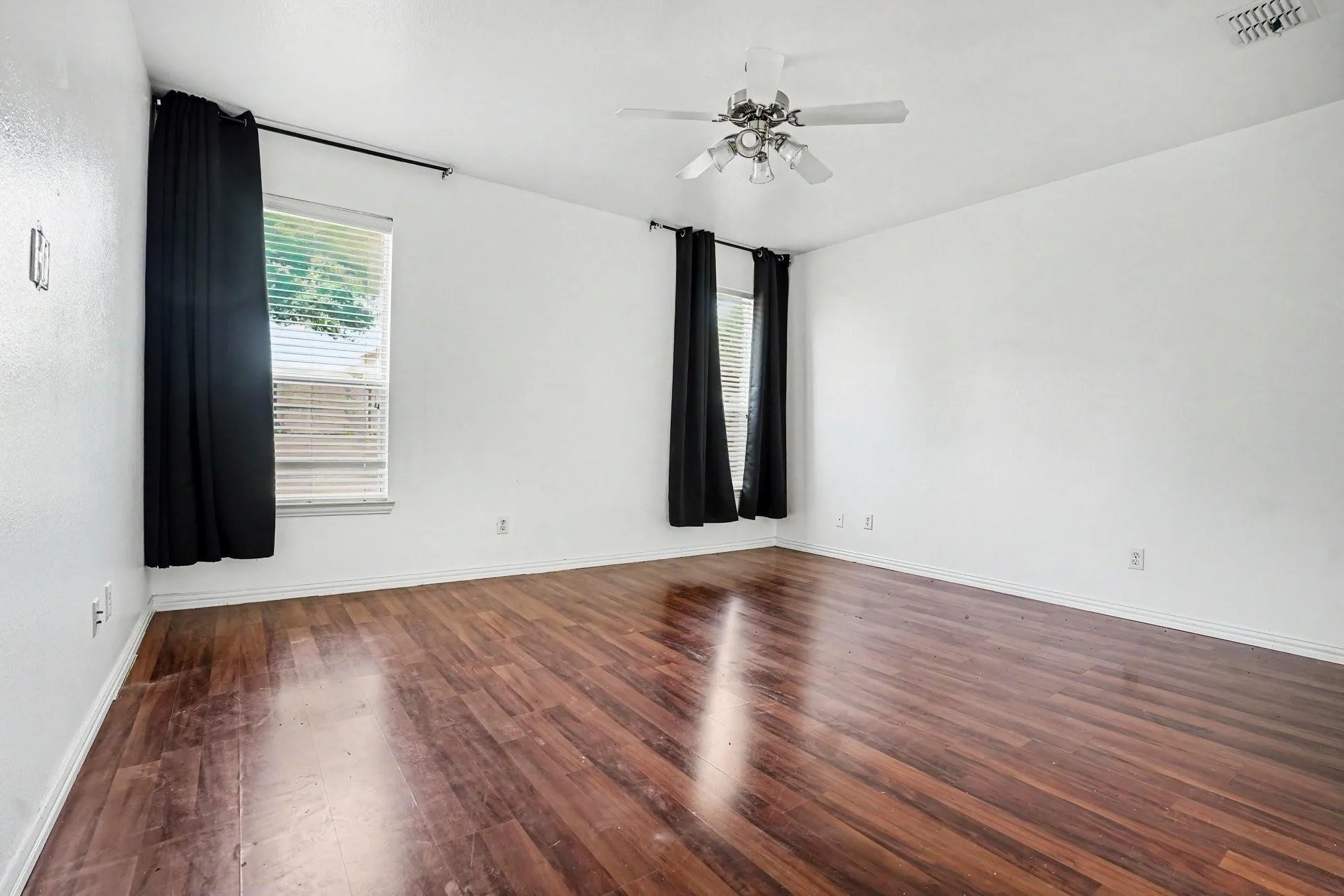 Spacious interior featuring wood-finish flooring, multiple windows with blinds, a ceiling fan, and white painted walls