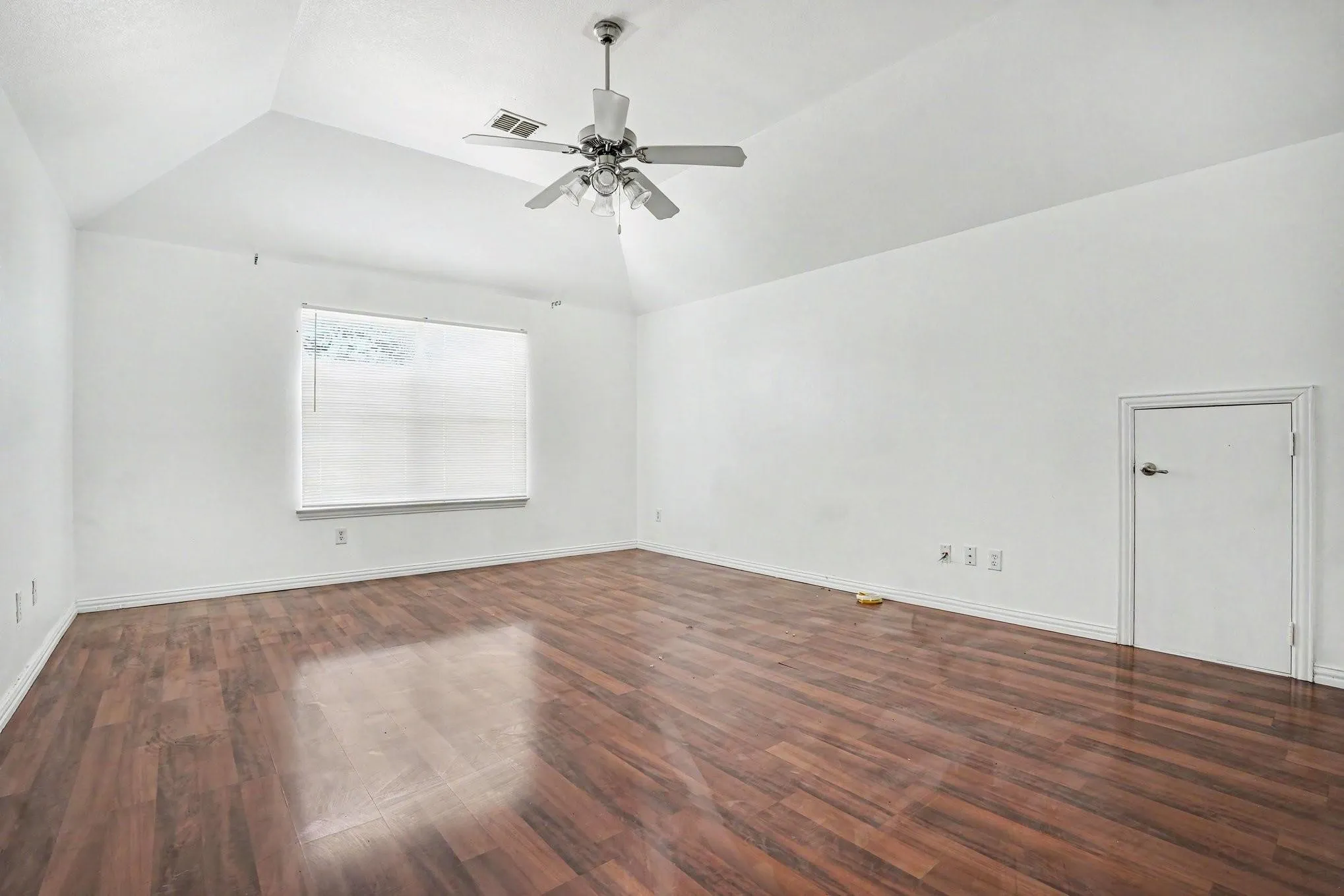 Vaulted ceiling featuring a ceiling fan with integrated lighting, wood-finish flooring, and a window with blinds