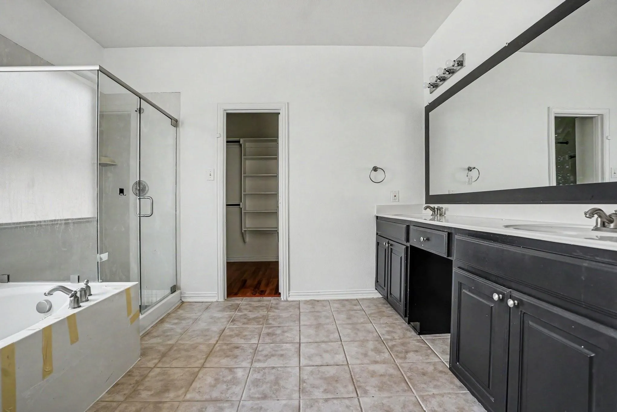 Dual vanity with undermount sinks, an expansive wall mirror, a separate glass-enclosed shower, and a built-in tub