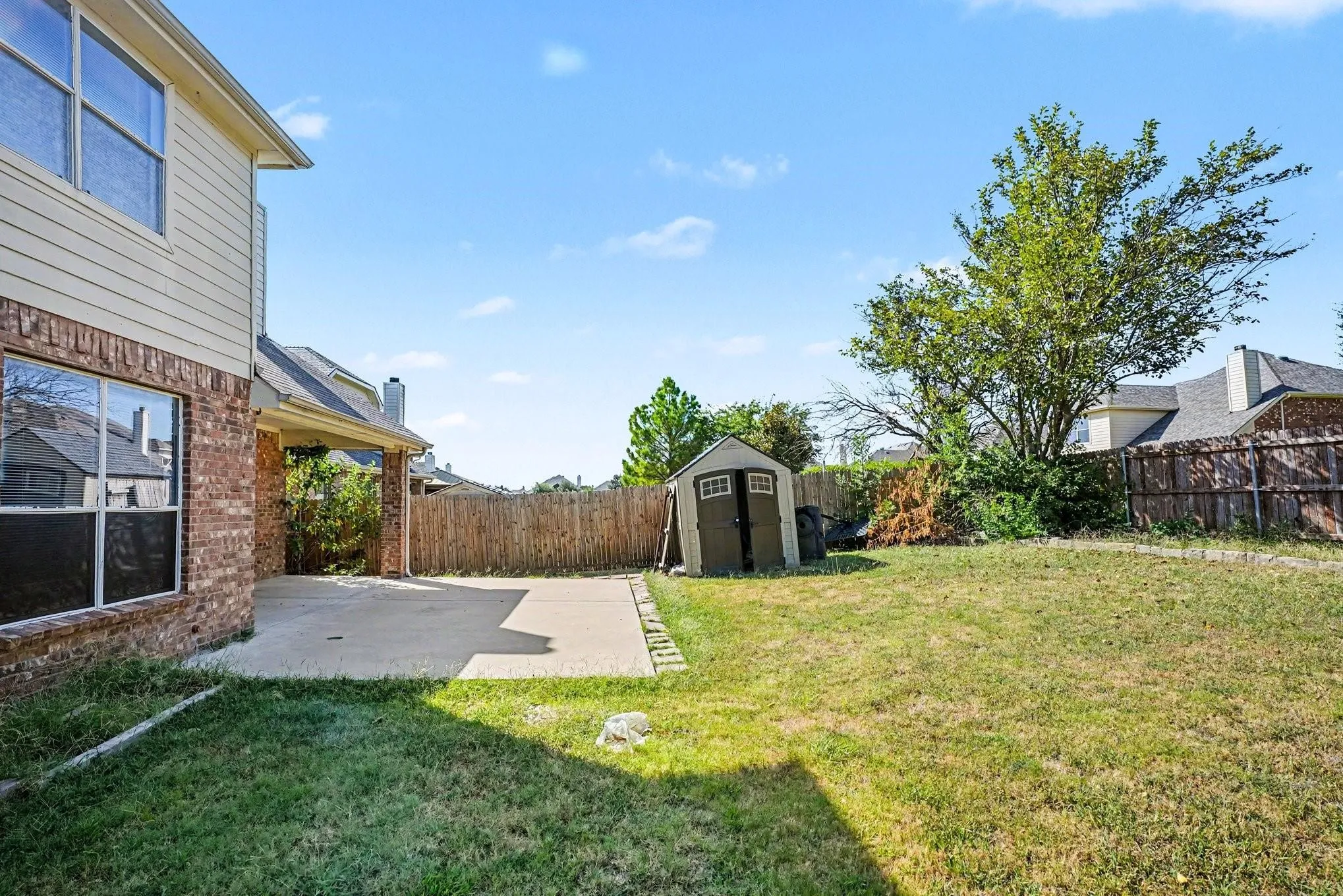 Expansive backyard featuring a wood privacy fence, concrete patio, and a storage shed