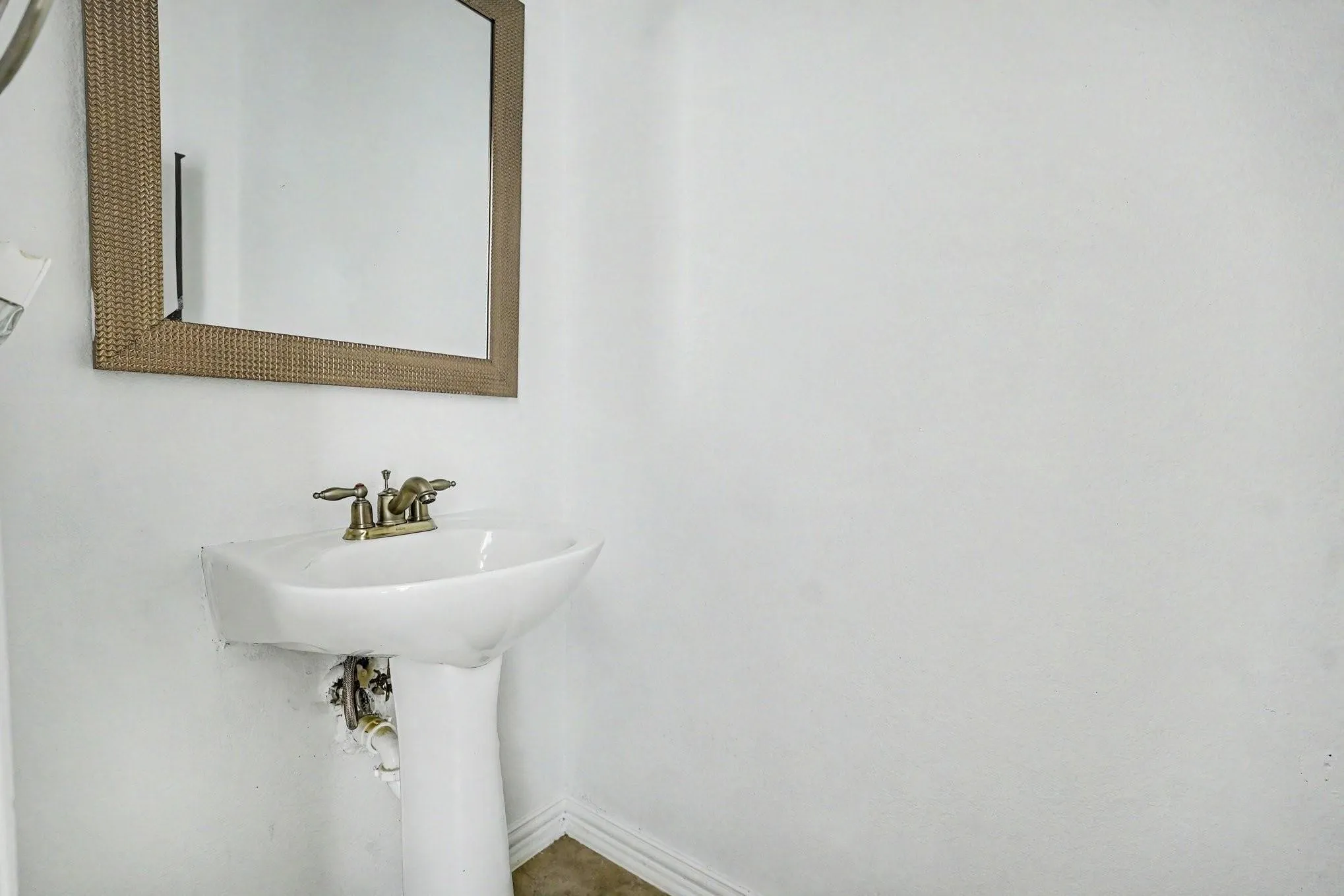 Pedestal sink with a brass-finish faucet, accompanied by a framed wall mirror