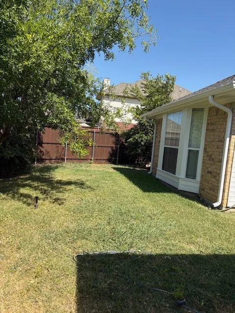 Expansive backyard featuring a manicured lawn, established trees, and a durable privacy fence