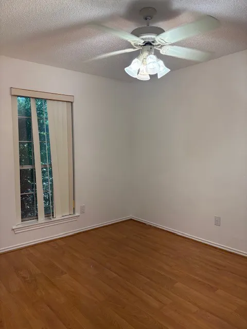 Wood-finish flooring, white walls, window with vertical blinds, and a ceiling fan with integrated lighting