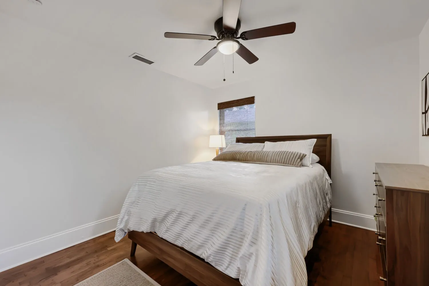 Wood-finish flooring, ceiling fan with integrated lighting, window with wood-toned blind, white painted walls, and white trim