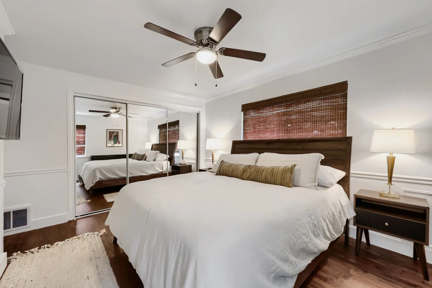 Hardwood flooring, crown molding, wall paneling, ceiling fan, and mirrored closet doors
