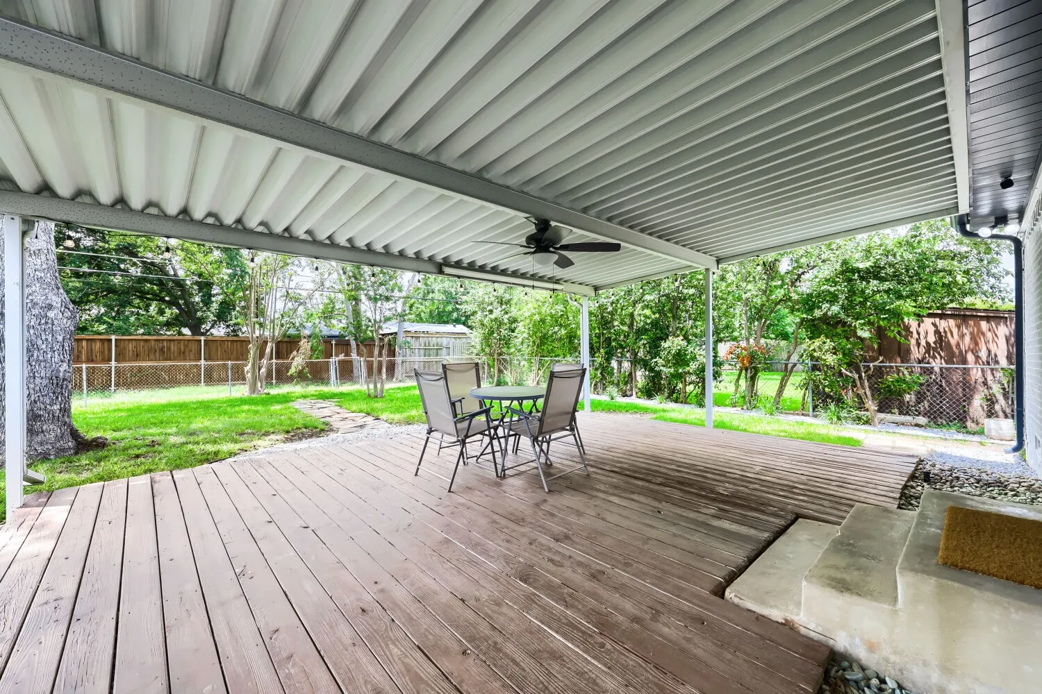Expansive covered patio featuring a wood-finish deck, ceiling fan, and concrete steps leading to the yard