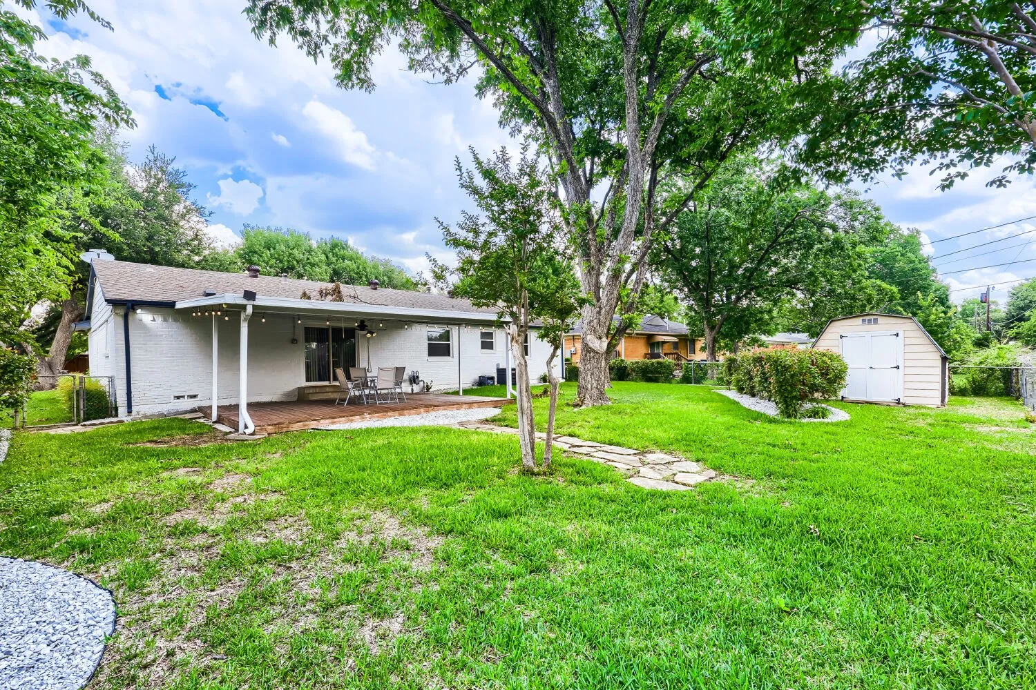 Expansive rear yard featuring a covered patio, wood-finish decking, and a detached storage shed