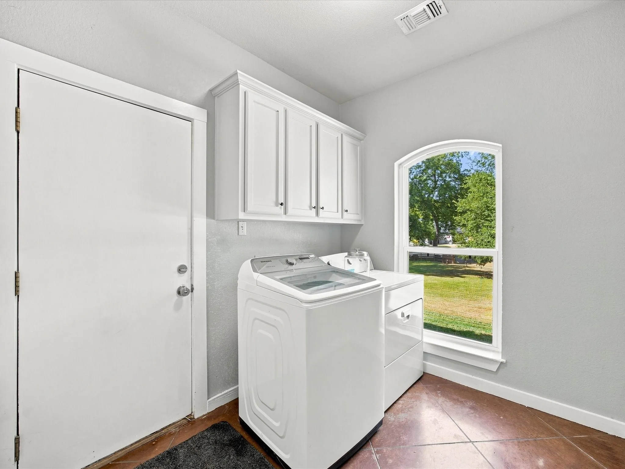 White shaker-style cabinetry, arched window, and durable flooring