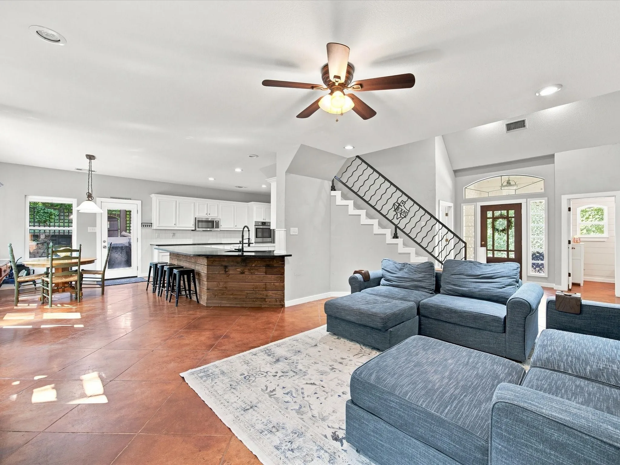 Expansive living area with wood-finish flooring, a contemporary kitchen island featuring a wood-panel base, white cabinetry, and a ceiling fan